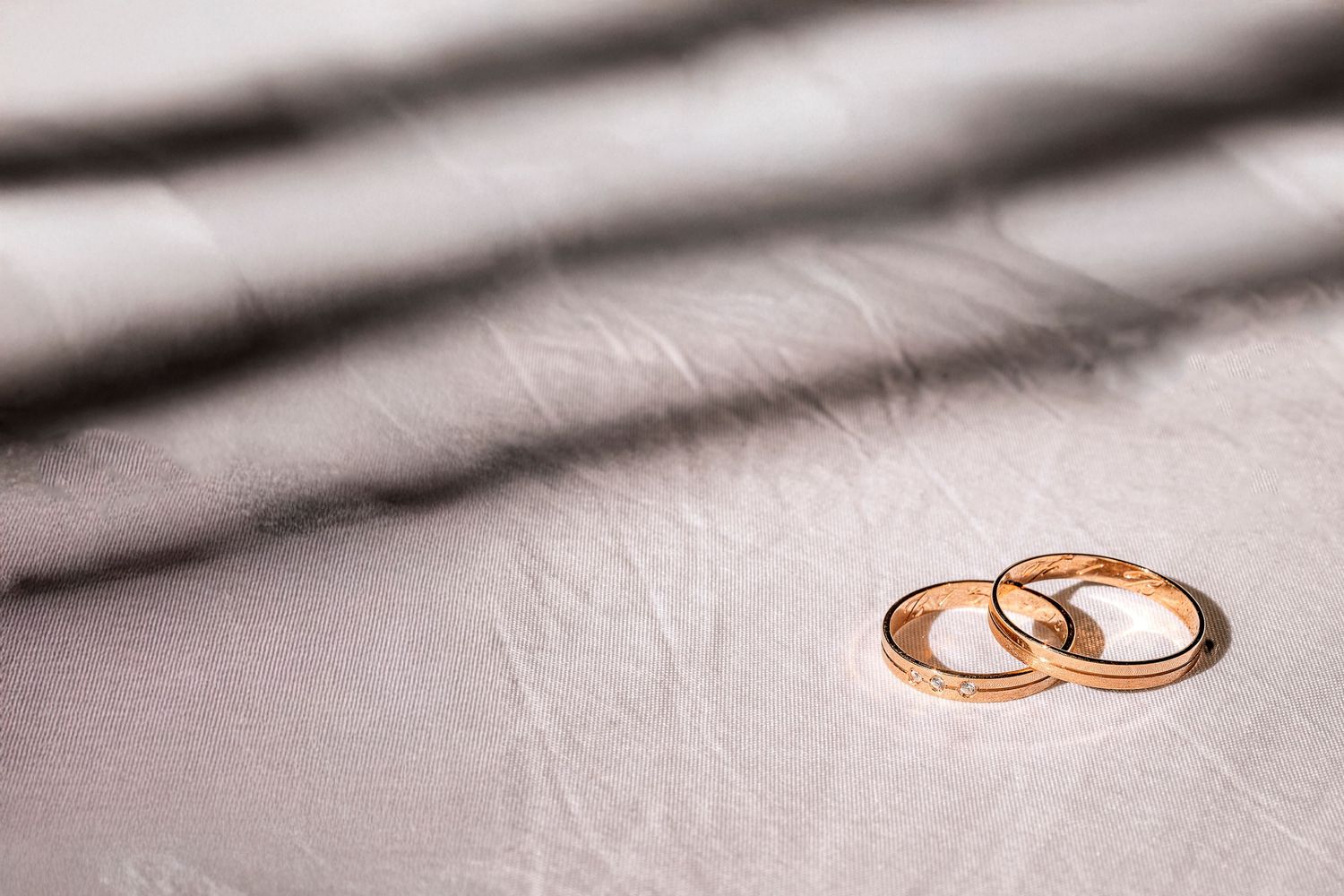 Two golden wedding rings sit on a soft gray textured surface in elegant lighting.