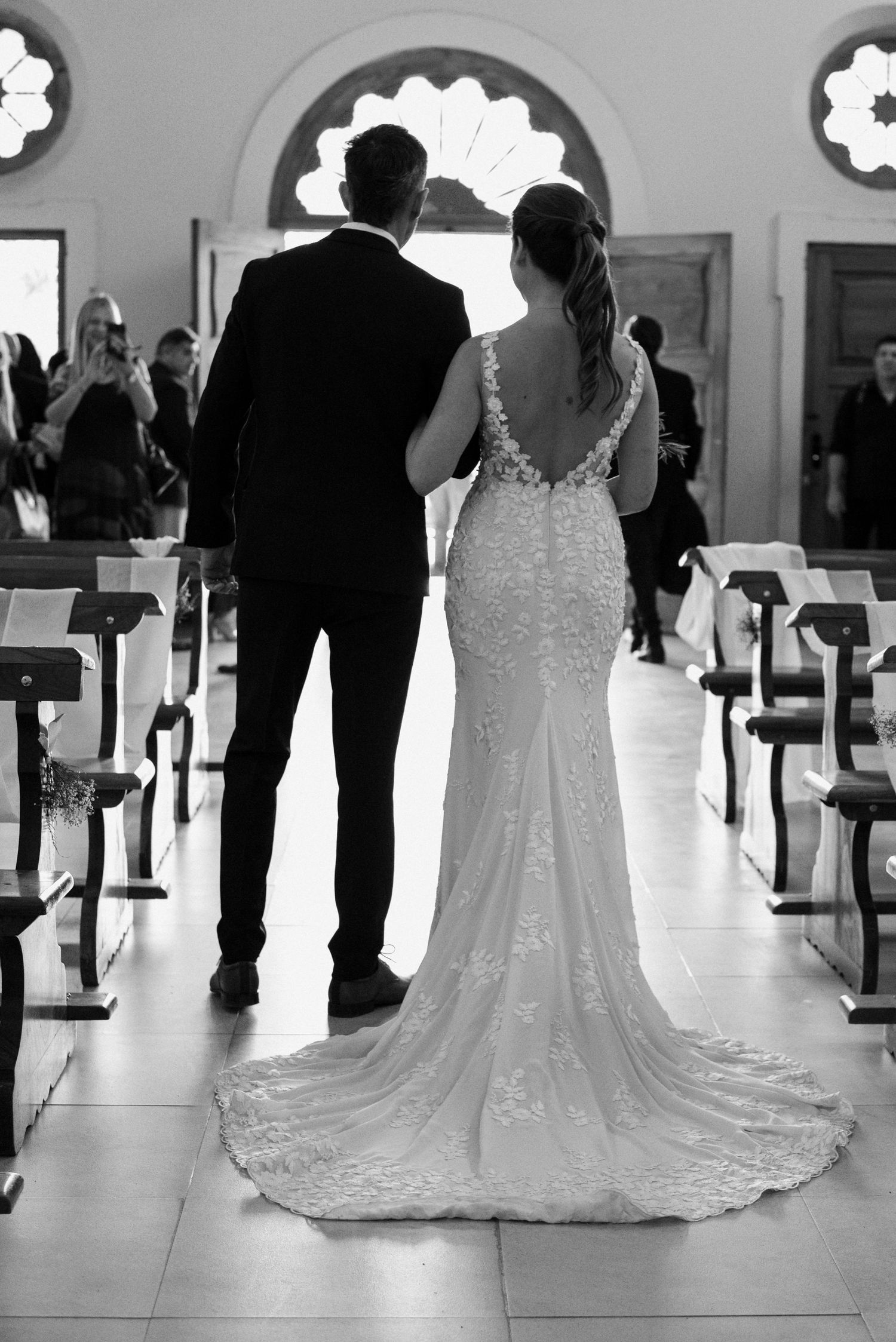 Black and white photograph of a wedding ceremony in a church with guests seated in pews and flowing bridal gowns.