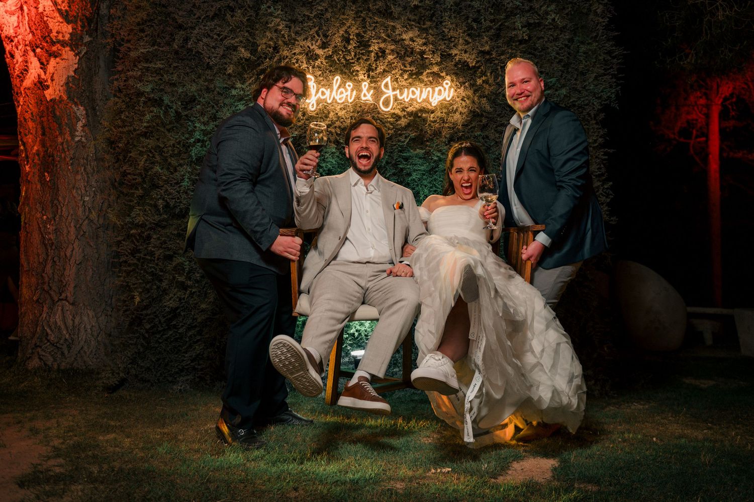 A romantic wedding couple sits together at dusk under trees illuminated by warm glowing lights. fotografos de boda en mendoza