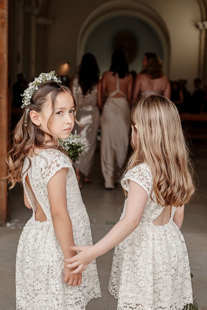 Two flower girls in white lace dresses with baby's breath flowers in their hair embrace at a wedding ceremony. wedding in mendoza