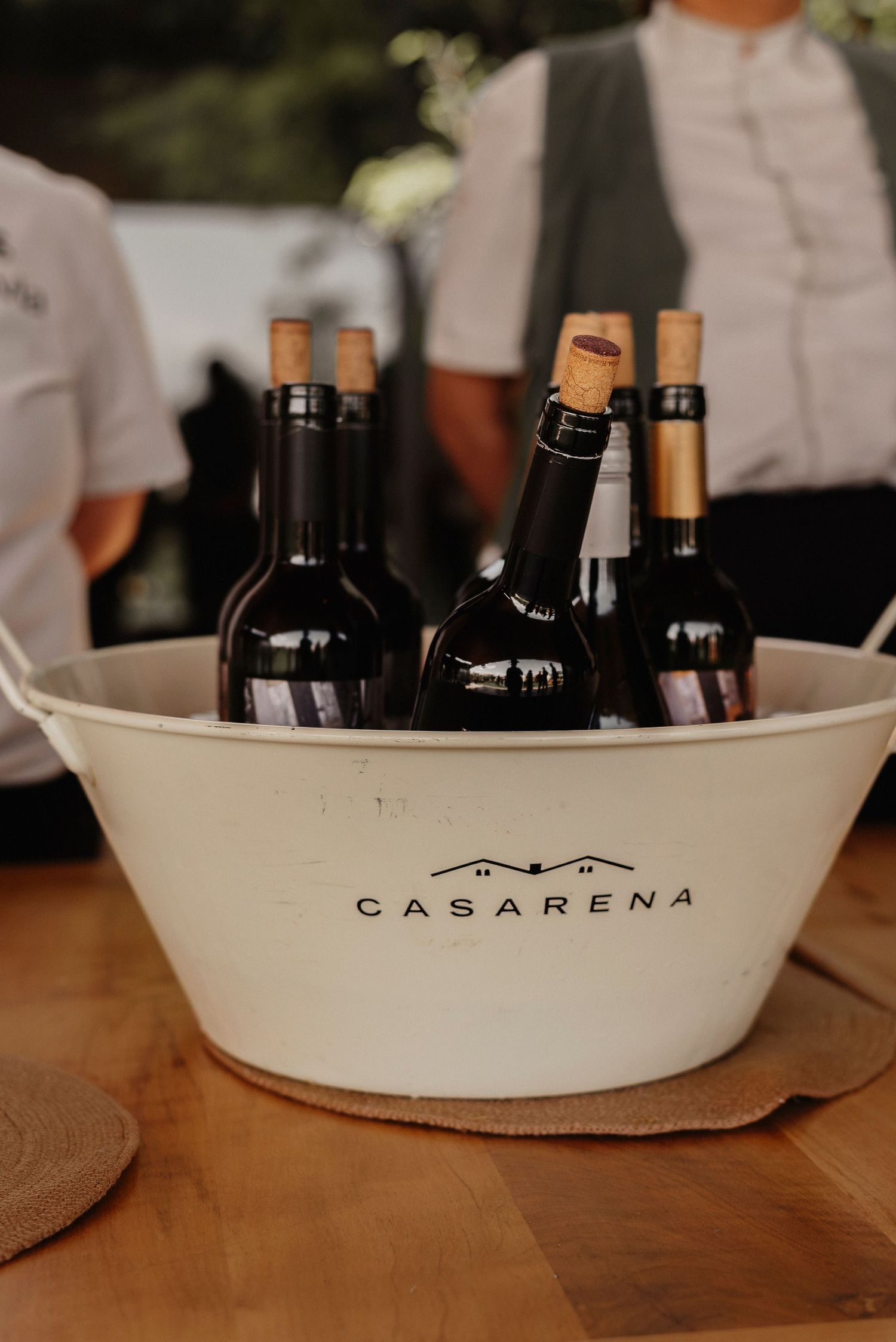 Wine bottles chilling in a white Casa Arena branded ice bucket on a wooden table at a restaurant.