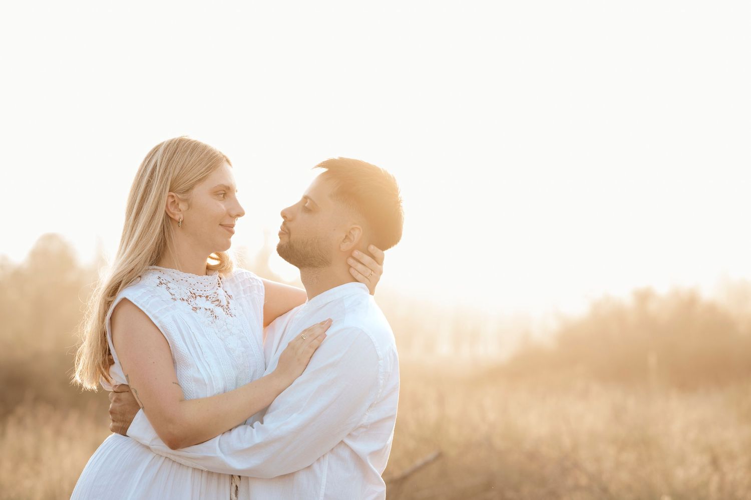 A couple embraces in a sunlit field during golden hour, with warm backlighting creating a romantic silhouette.