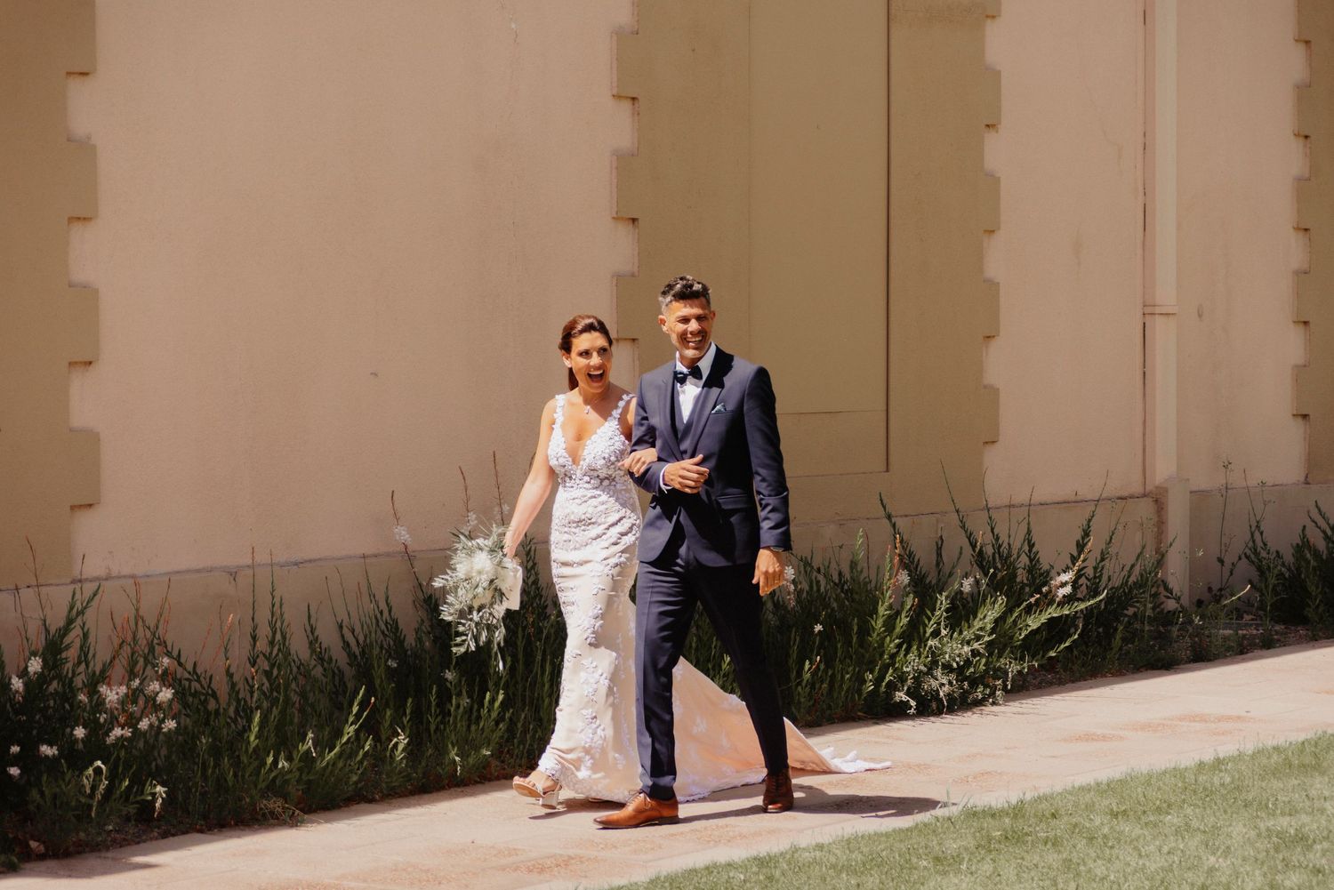 A couple in wedding attire walks along a beige wall with plants, creating a panoramic sequence of romantic moments.