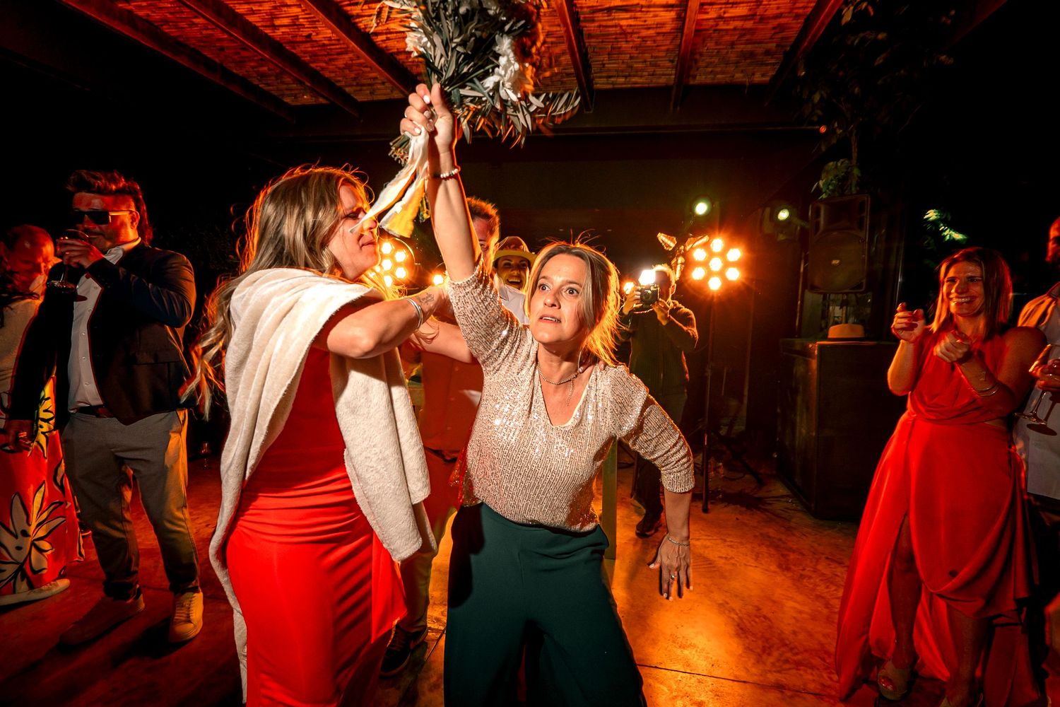Couples dancing together at a dimly lit wedding reception with red and amber lighting creating a romantic atmosphere.