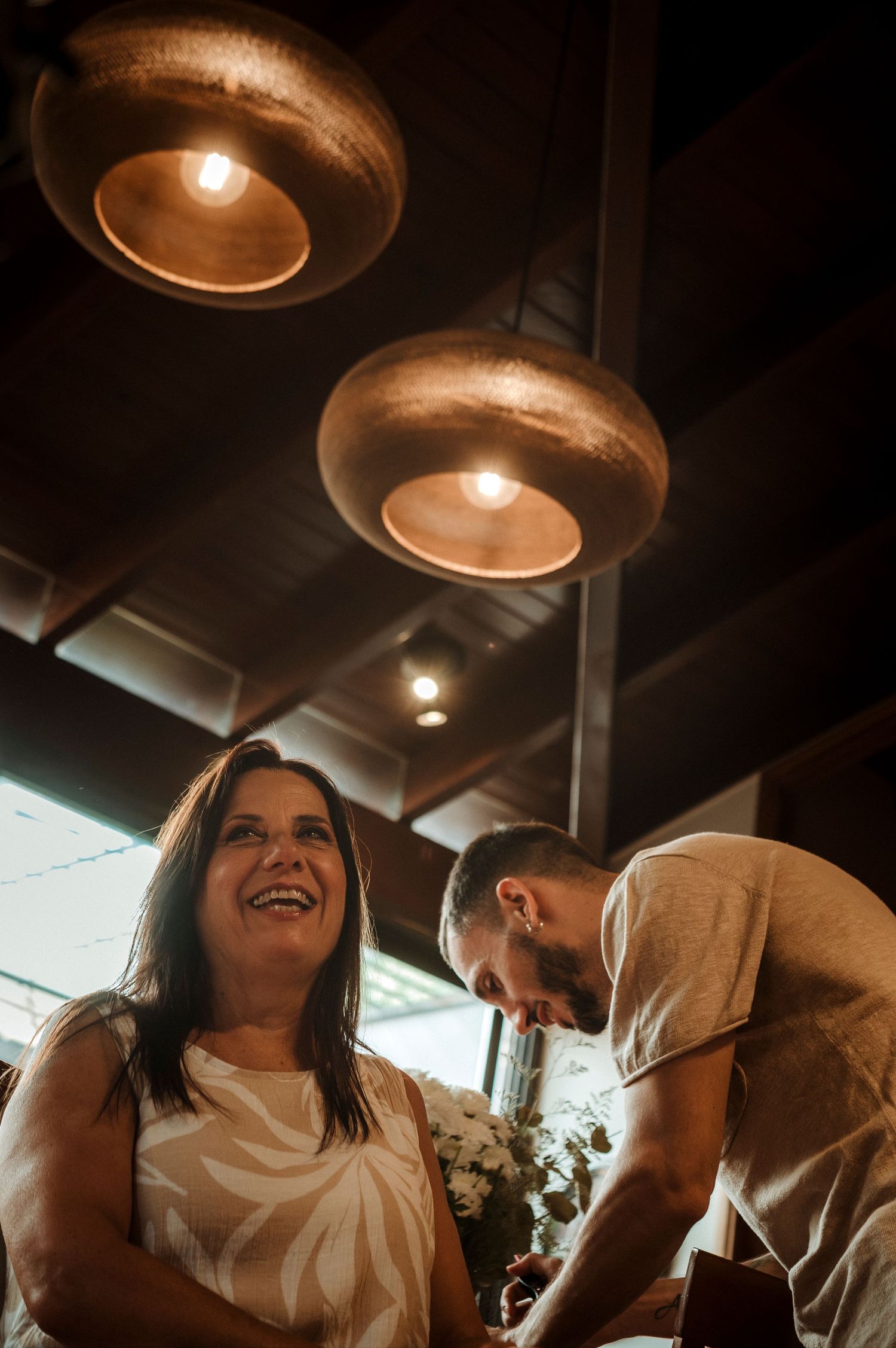 Two people share a joyful moment together under warm pendant lighting in what appears to be a restaurant or venue.