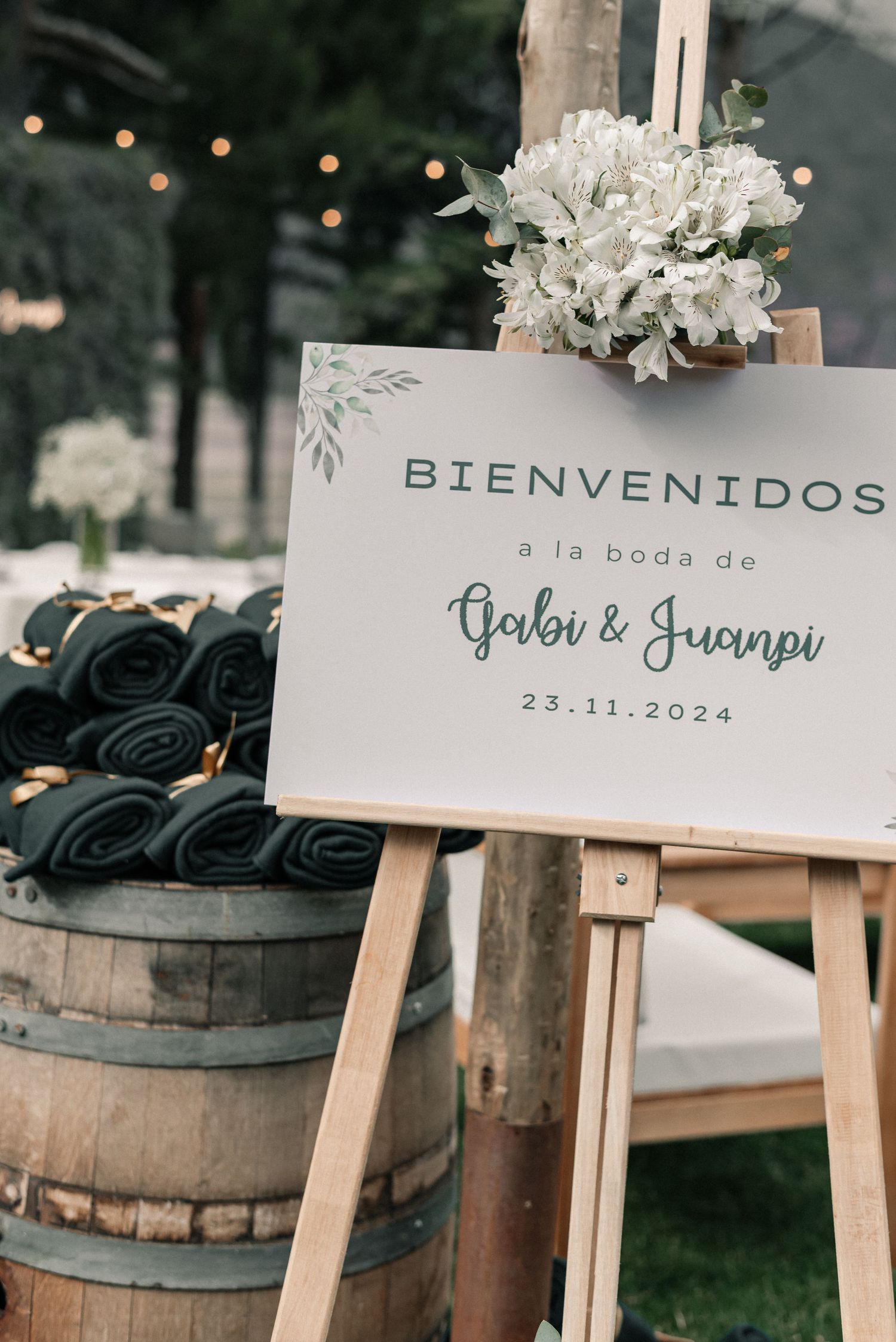 Rustic wedding welcome signs displayed on wooden easels with white flowers and decorative barrels in the background.