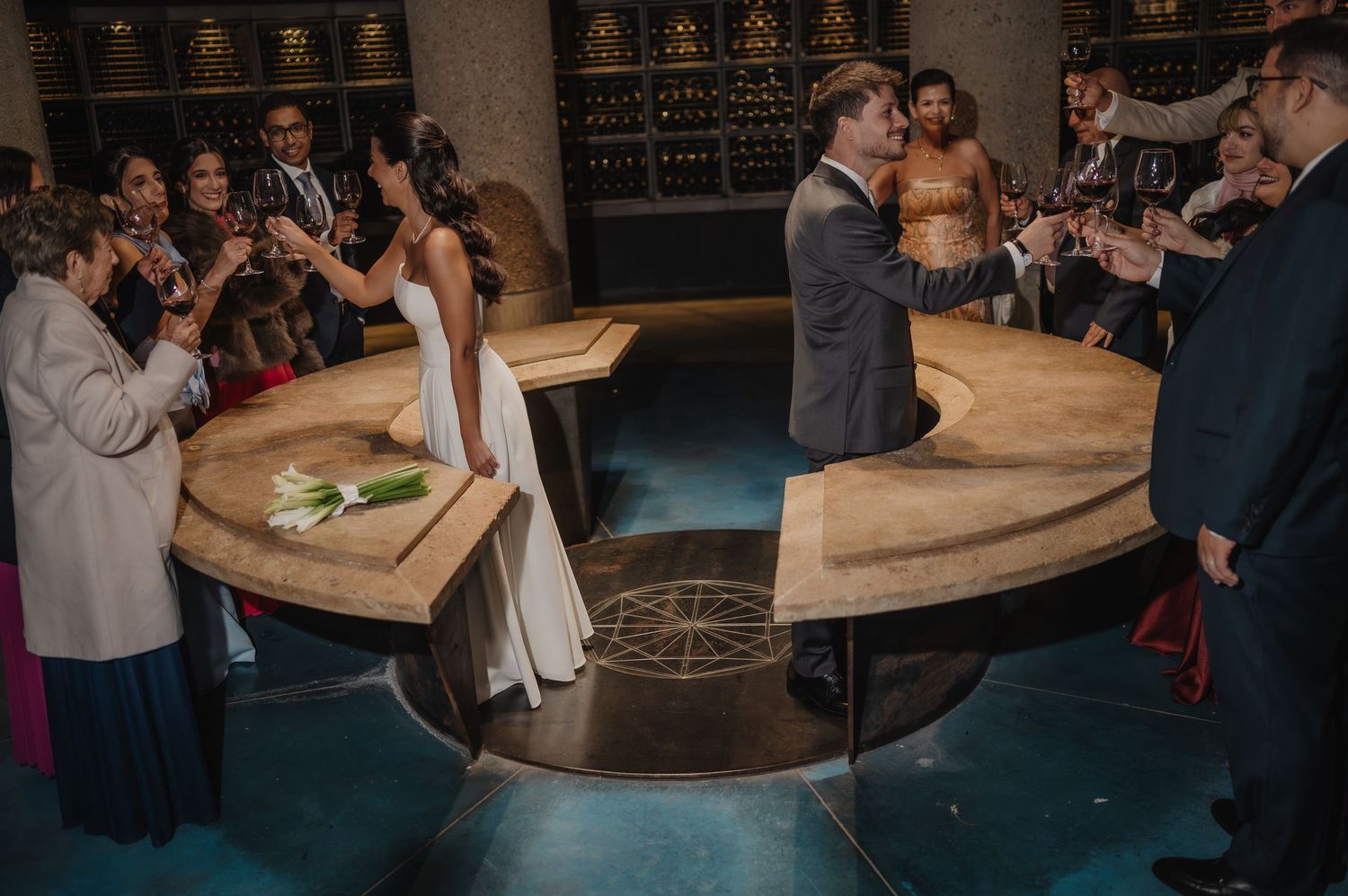 Bride and groom exchange vows at a circular altar surrounded by guests in an elegant venue.