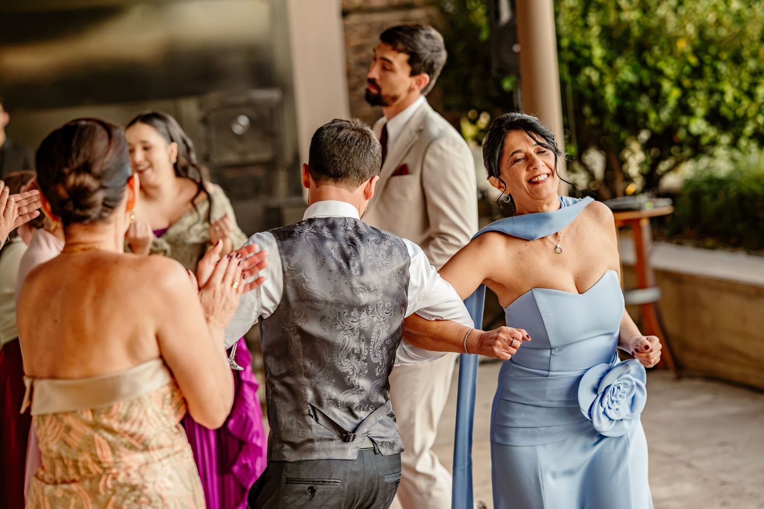 Guests dancing and celebrating joyfully at an outdoor wedding reception, woman in blue gown smiling.