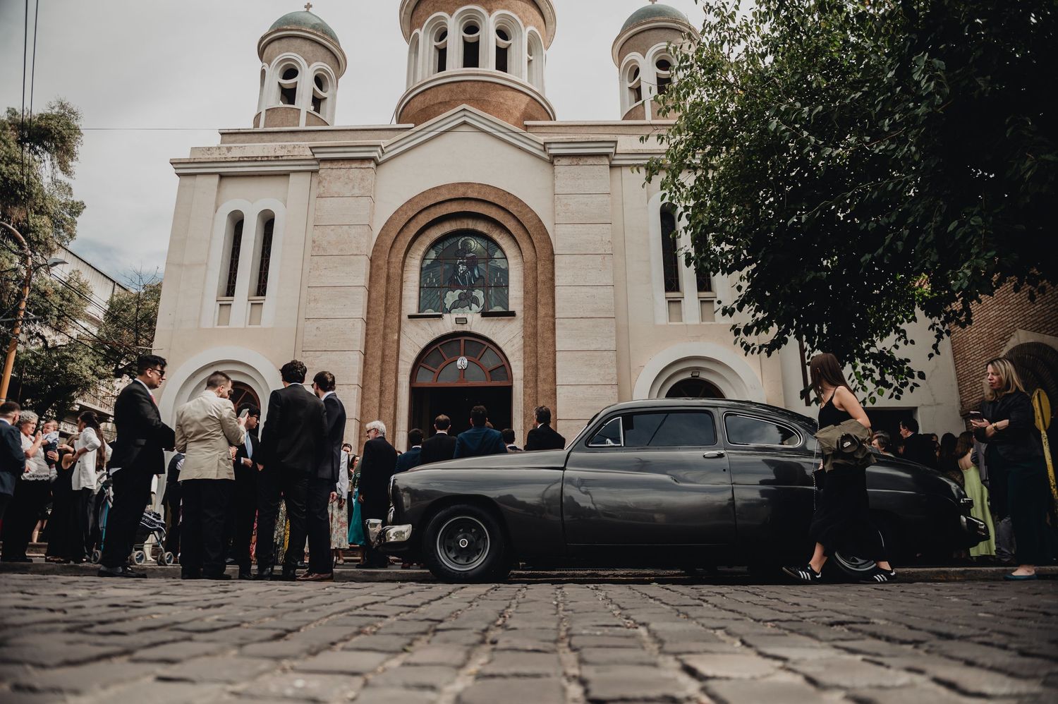 A vintage car parked outside an elegant white church with a classic architectural facade.