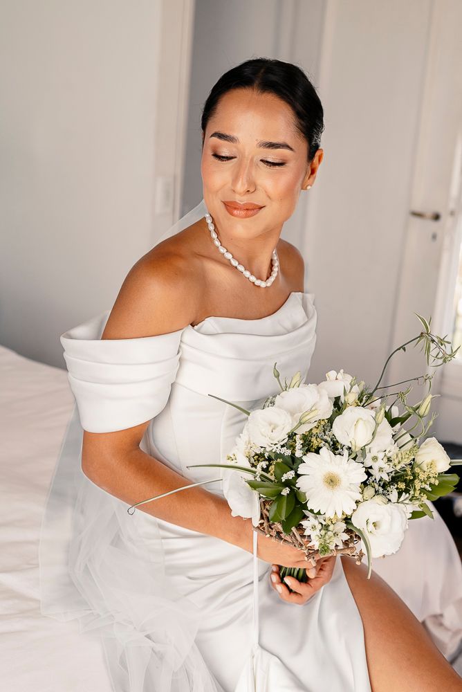 Bride in elegant off-shoulder white wedding dress holding a romantic bouquet of white flowers and greenery. wedding in mendoza