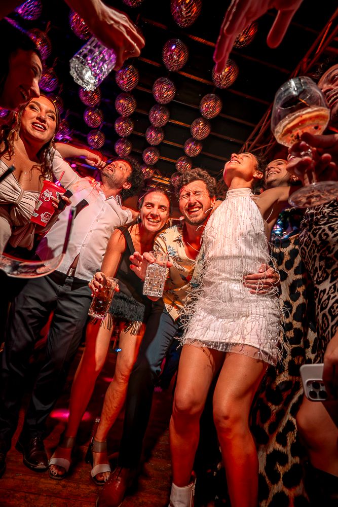 Party crowd dancing at a nightclub with disco ball lighting and festive outfits.