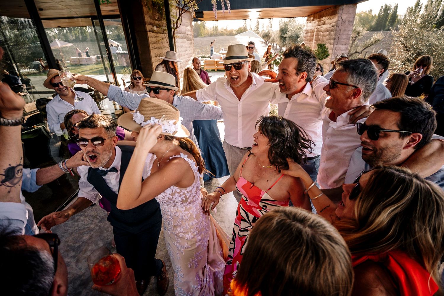 Wedding guests in white attire dance and celebrate during an outdoor reception party at sunset.
