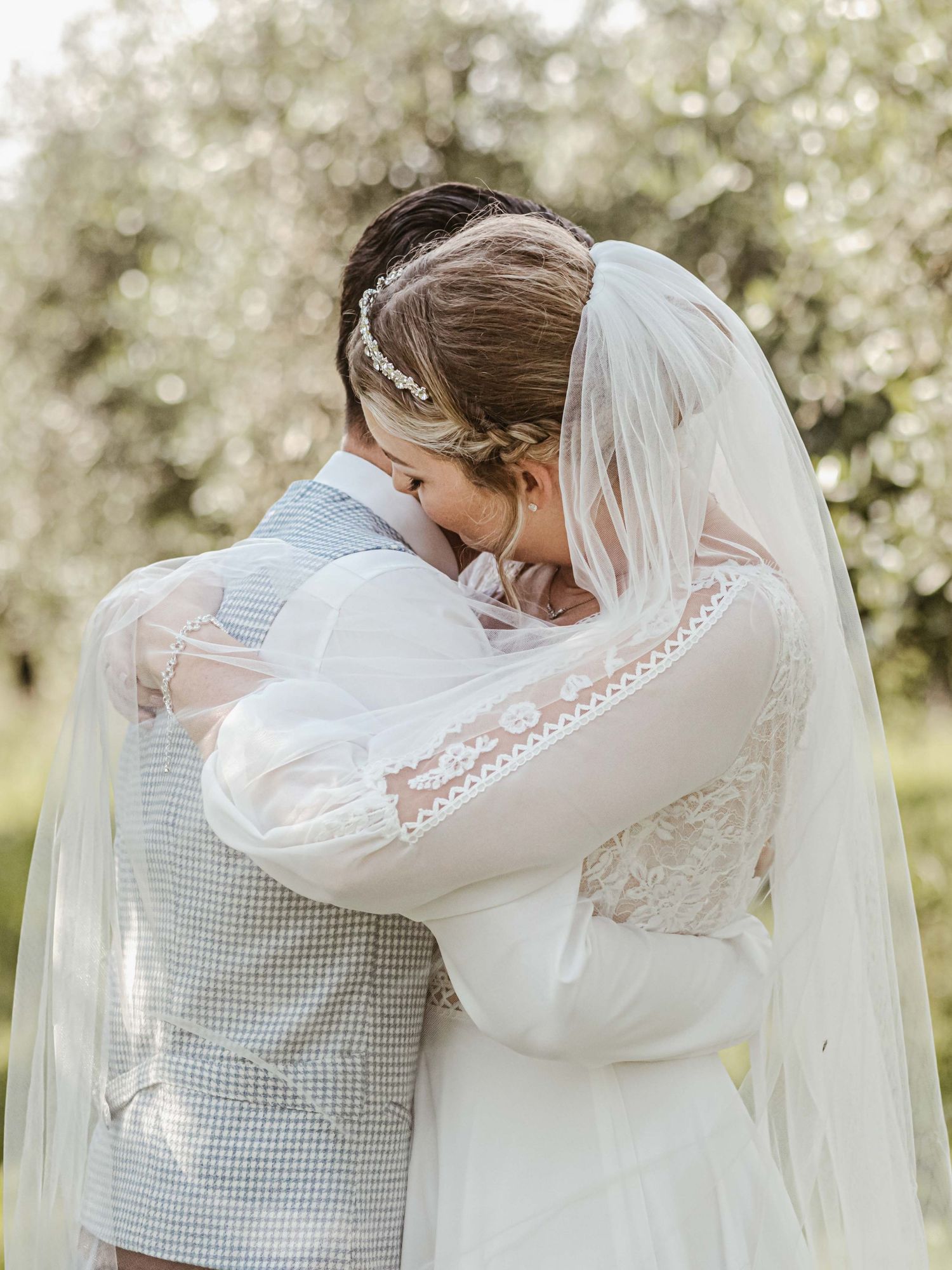 Tender embrace between newlyweds with the bride wearing a flowing lace gown and veil.