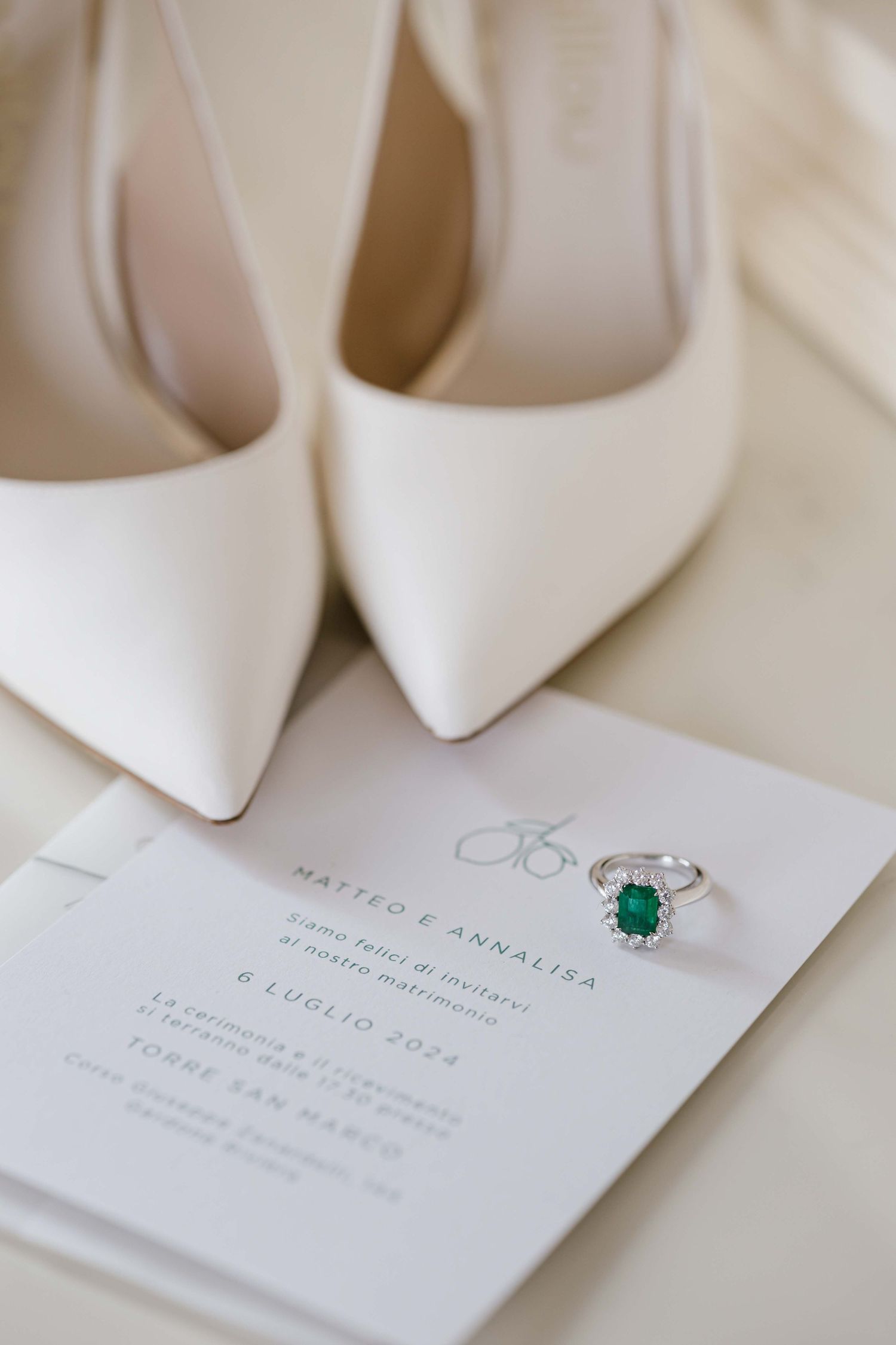 White bridal shoes and emerald ring displayed with elegant wedding invitation.