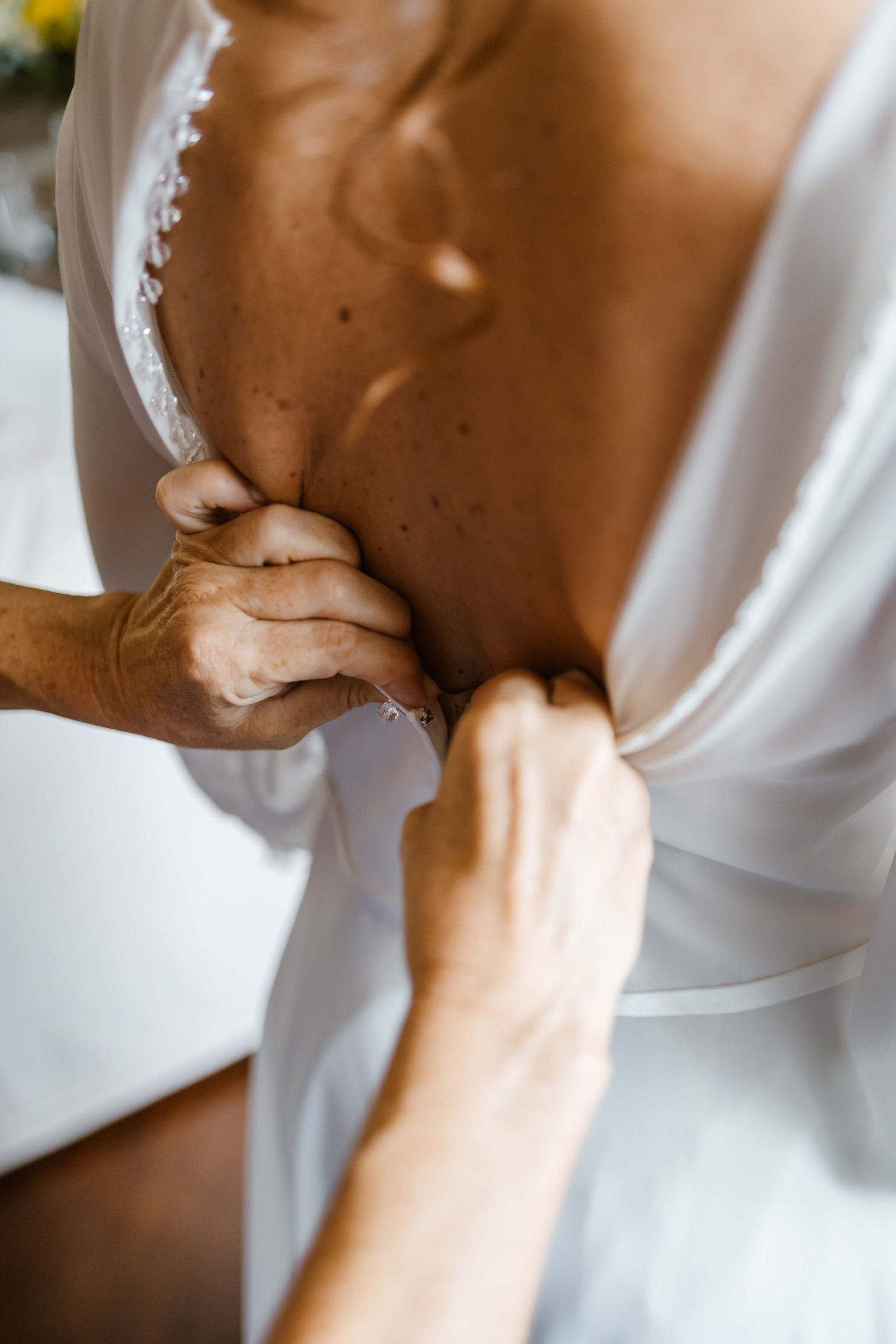 Close-up of hands adjusting a white wedding dress during preparation.