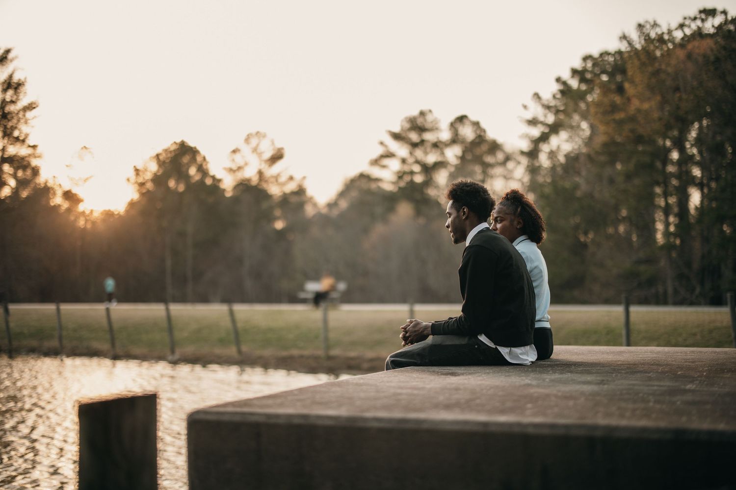Couple sitting on a concrete ledge by a Suwanee lake at sunset, candid Atlanta engagement photography, black atlanta photography