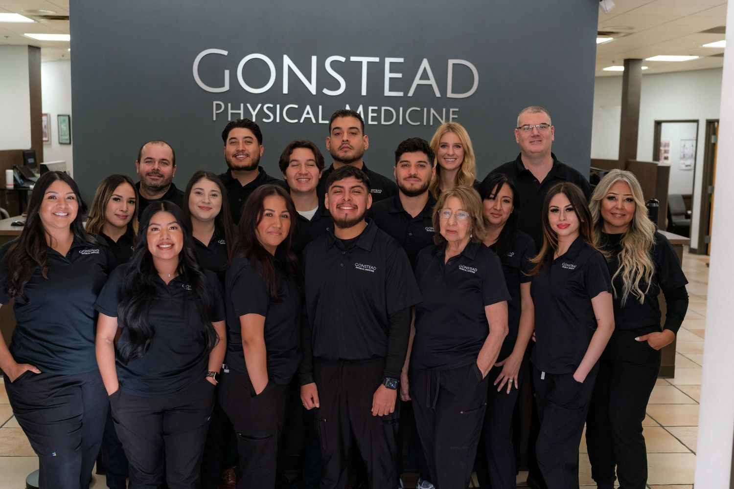 A group of medical professionals in black uniforms standing together in front of a Gonstead Physical Medicine sign.