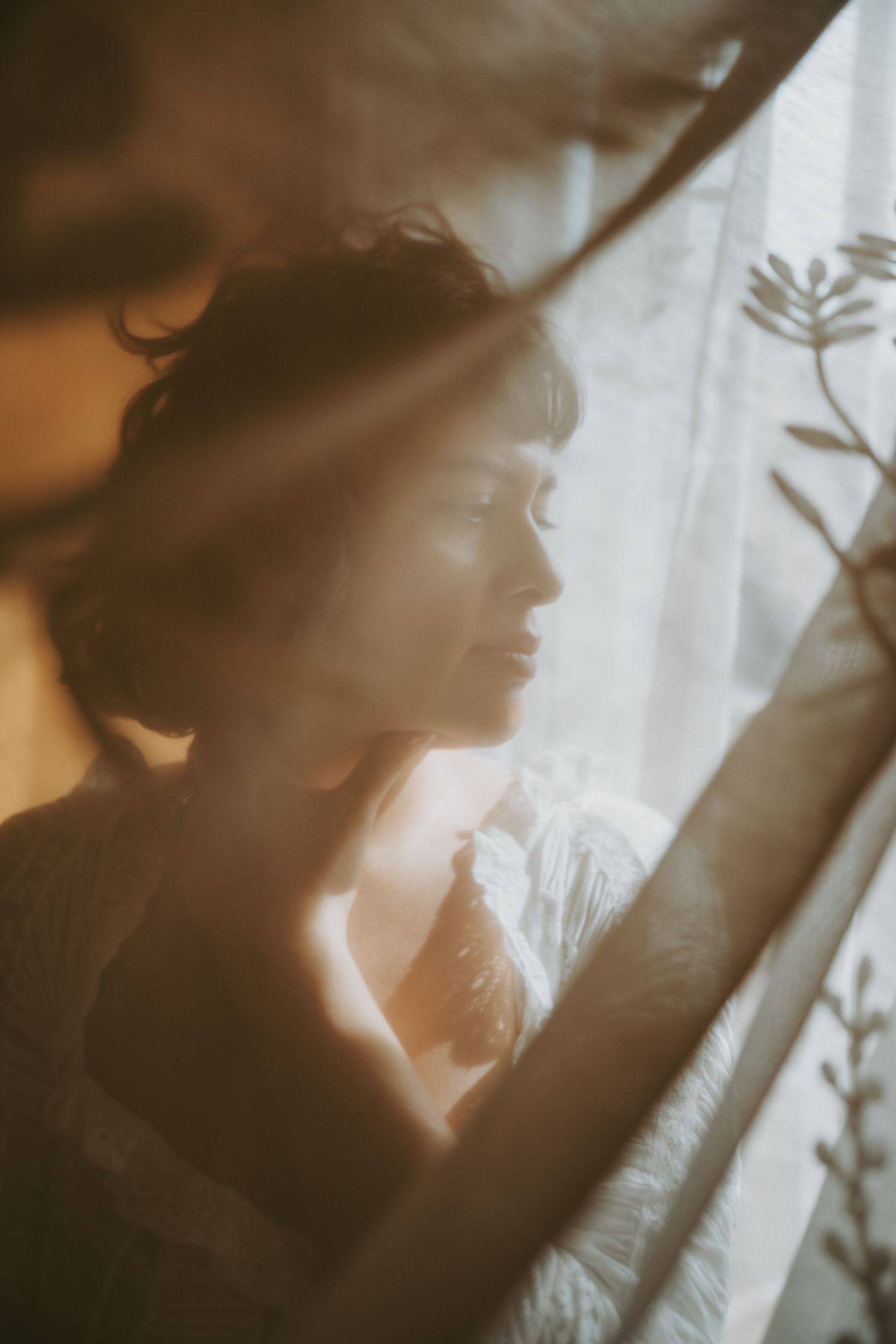 Dreamy silhouette profile by window with soft natural light and sheer curtains creating ethereal atmosphere.