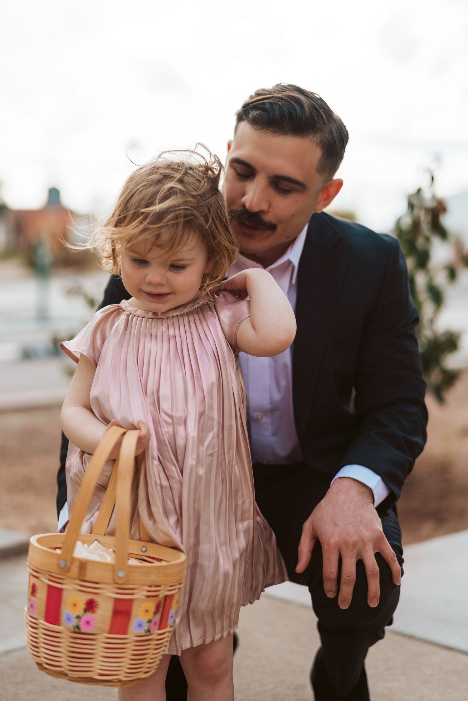 Small child in pink dress holds wicker basket at formal event.