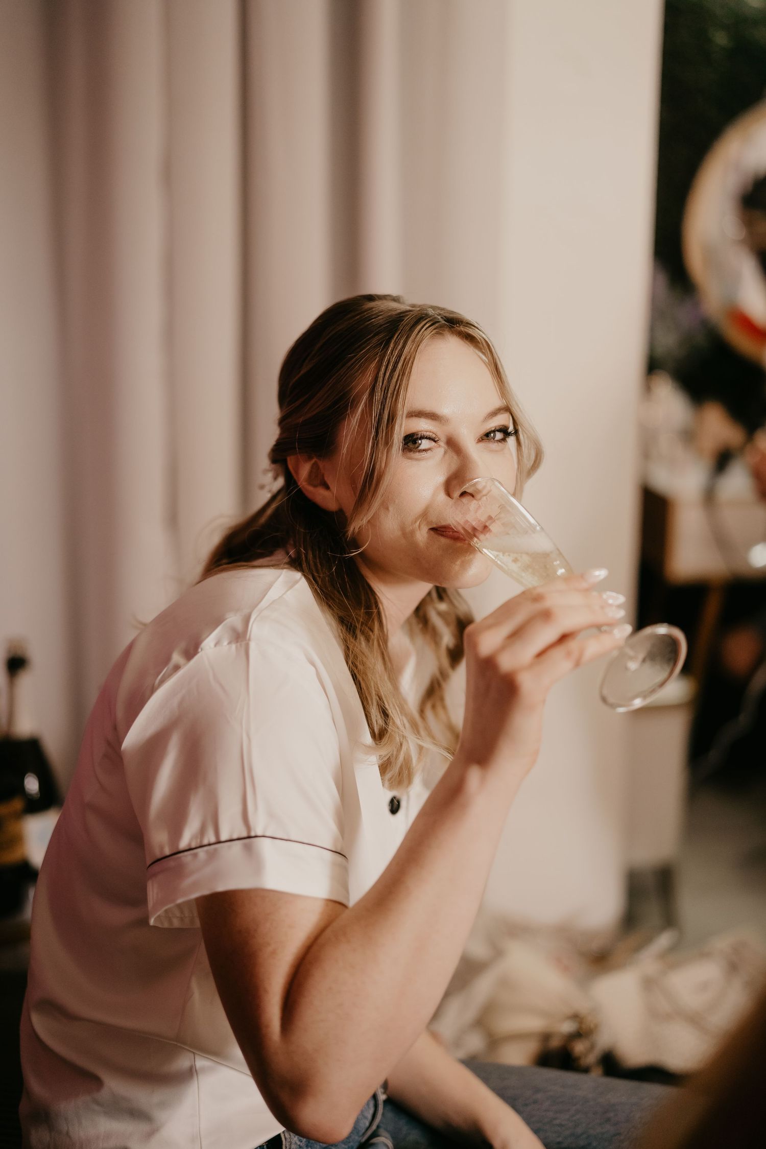 Person in pink satin shirt enjoying champagne during wedding preparations.