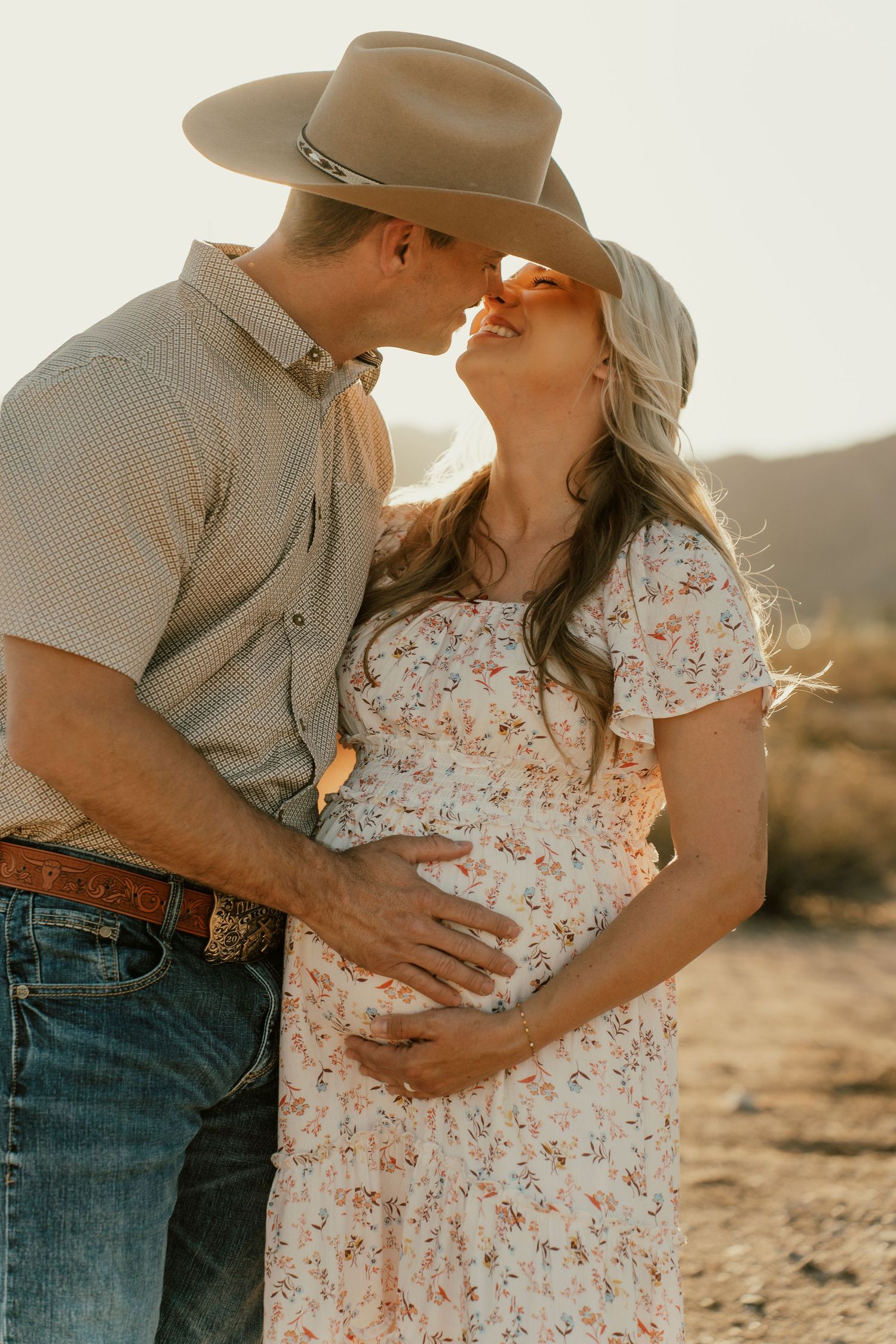 Romantic desert maternity photo with couple sharing intimate moment in western attire.