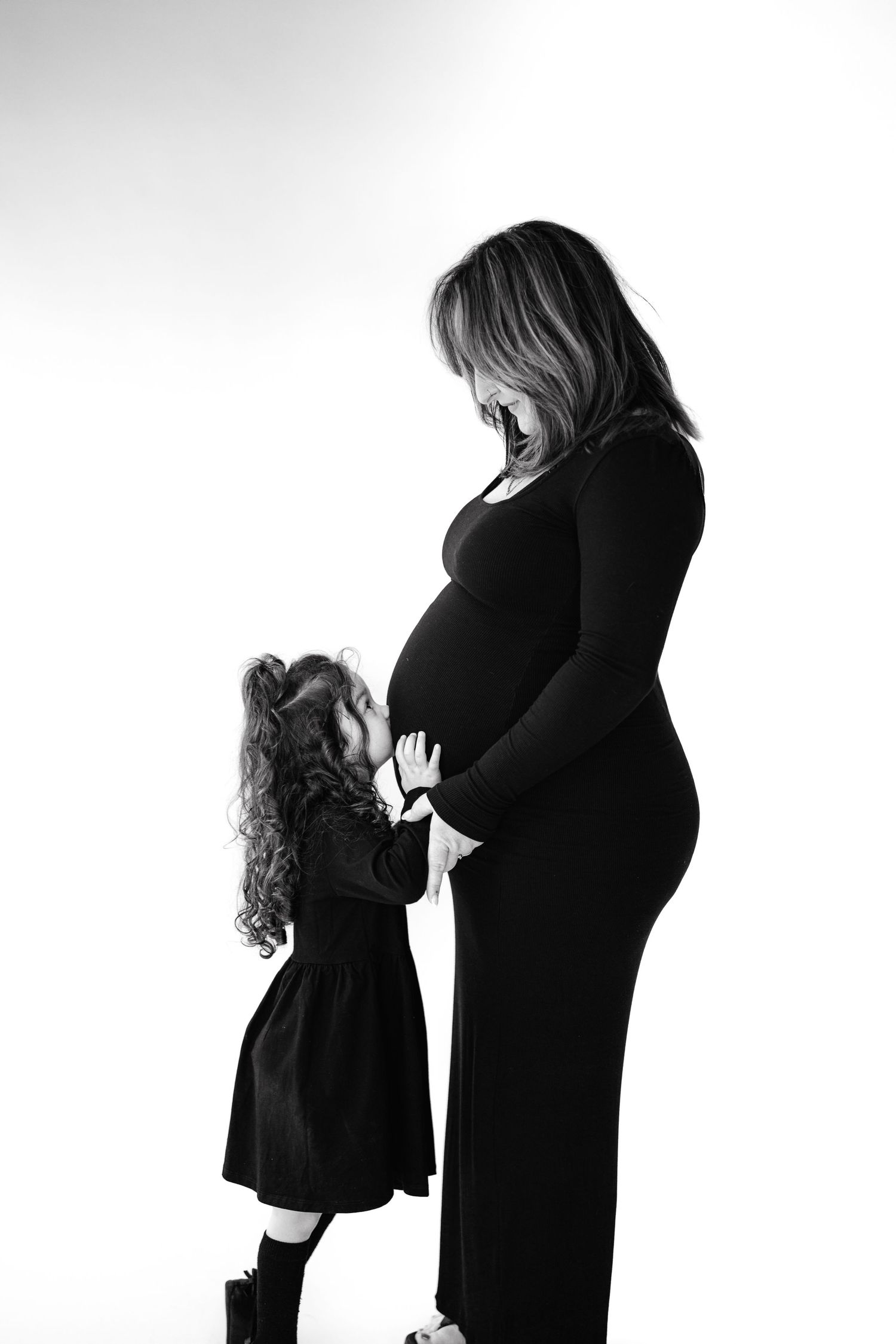 Silhouette of a child touching their mother's pregnant belly in a black and white portrait.