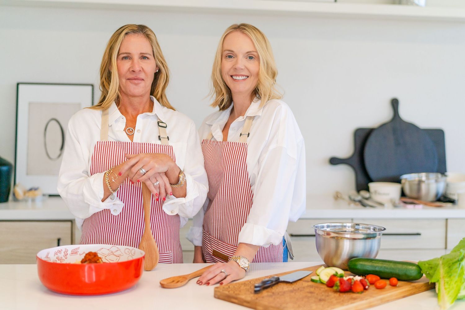 Two people in white lab coats examine food ingredients and beverages in a bright modern kitchen setting.