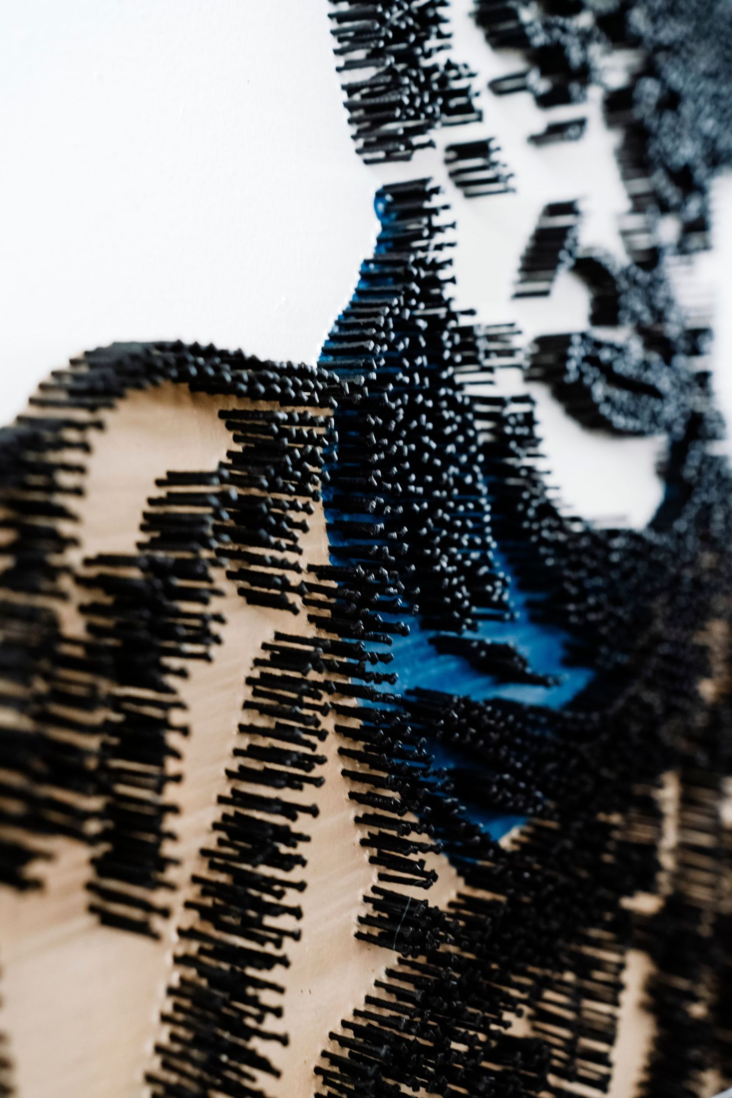 Close-up of an art piece made with black pins creating textural patterns with blue accents.