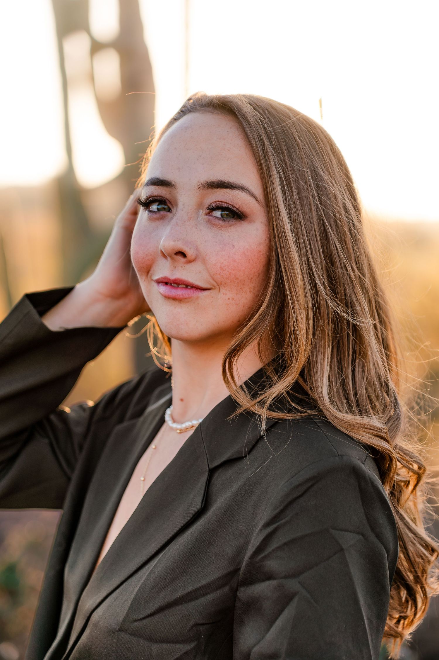 Portrait of person wearing black blazer with gold earrings in warm sunset lighting.
