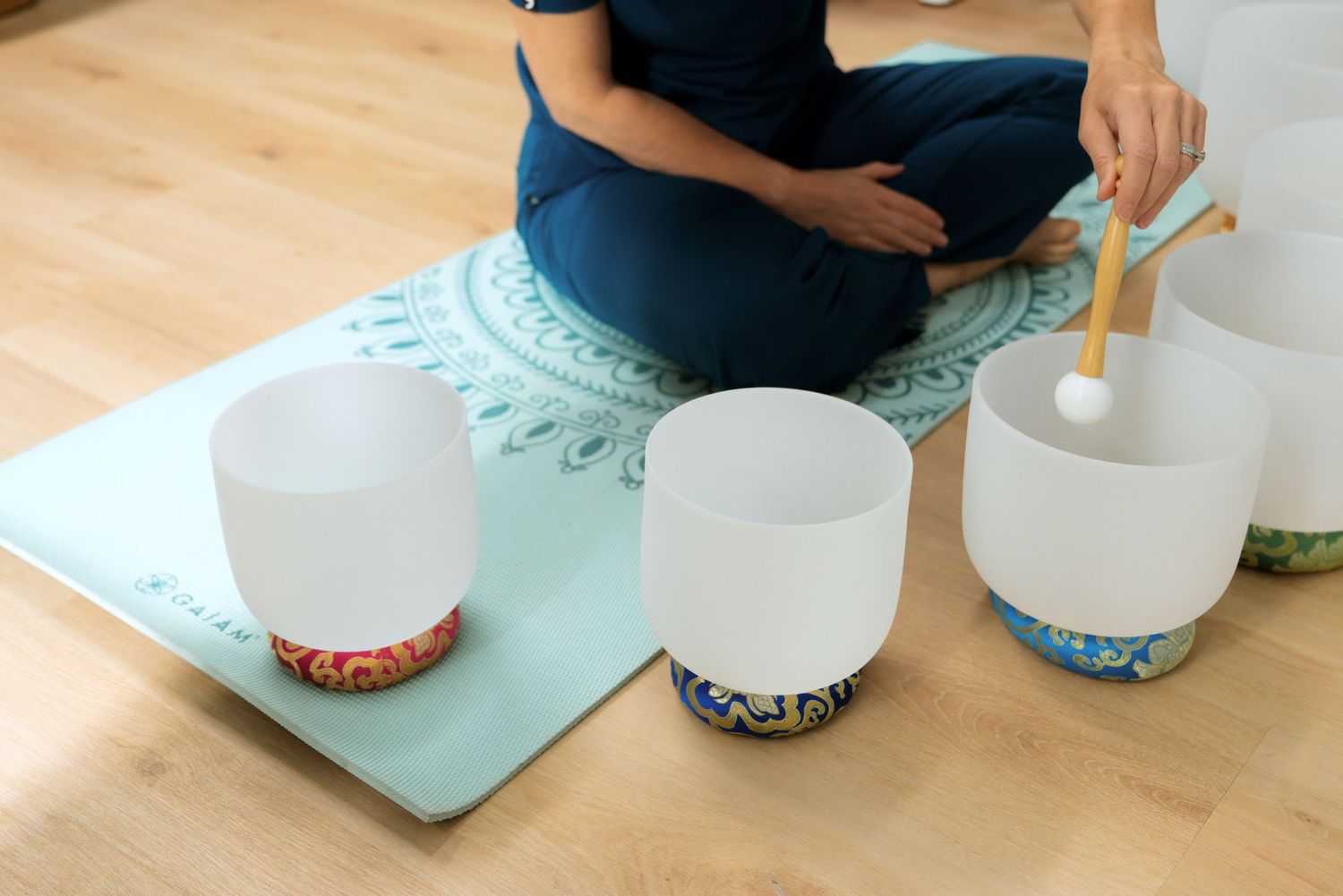Hands pouring liquid into multiple clear glass cups arranged in a row on a white surface.