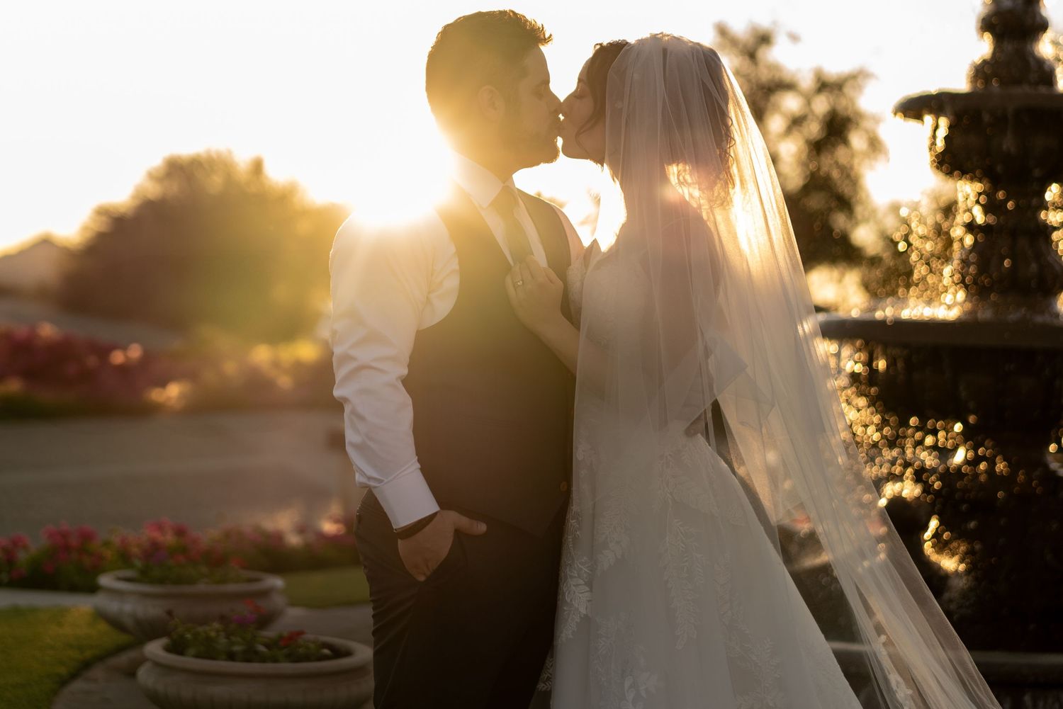 Newlywed couple silhouetted against golden sunset near garden fountain.