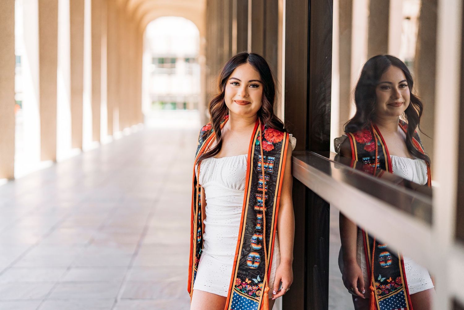 Sunlit graduation photos in maroon academic regalia along colonnade walkway.