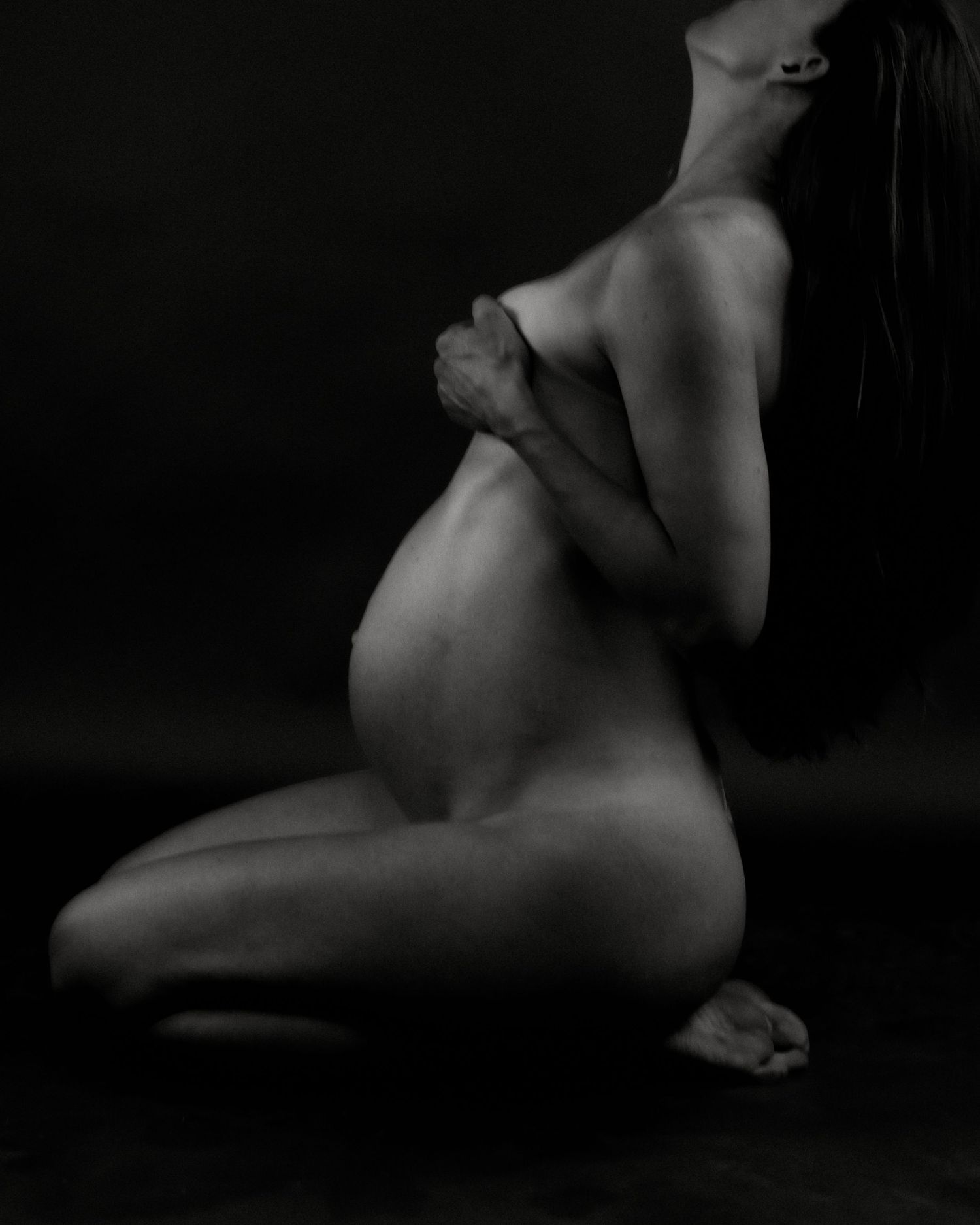 Artistic black and white silhouette photography series showcasing the curves of pregnancy against a dark background.