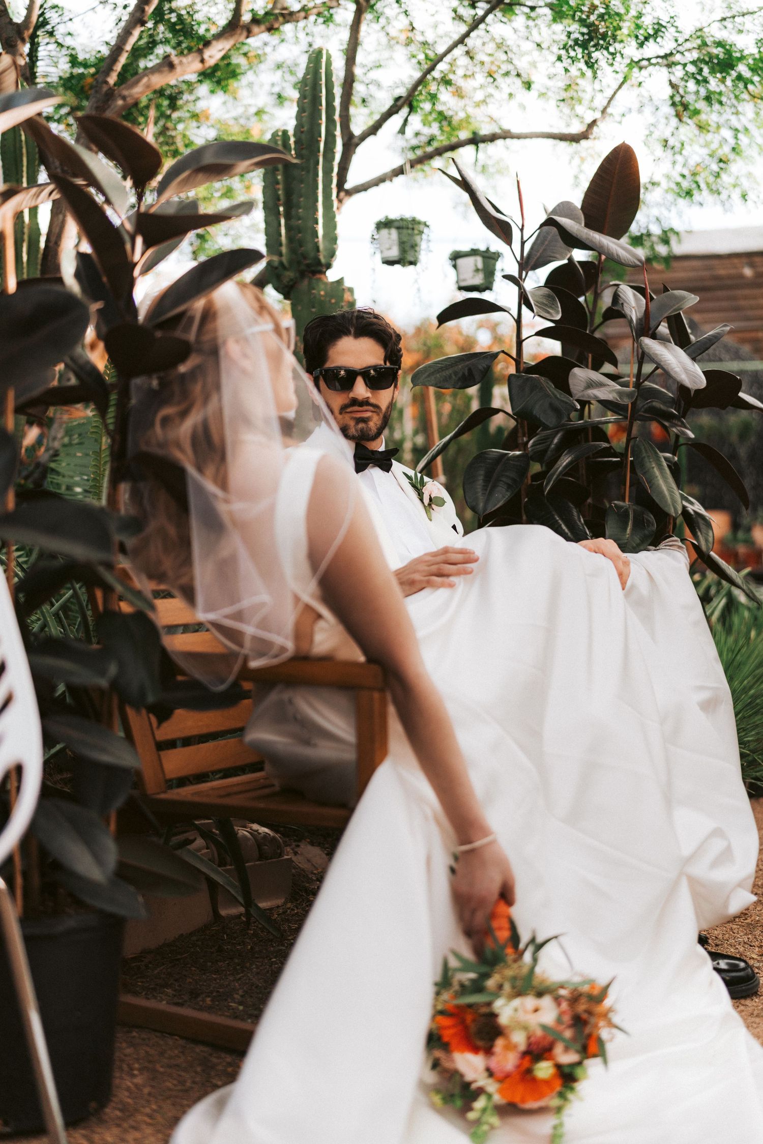 Wedding scene in lush garden setting with white dress flowing among tropical plants.