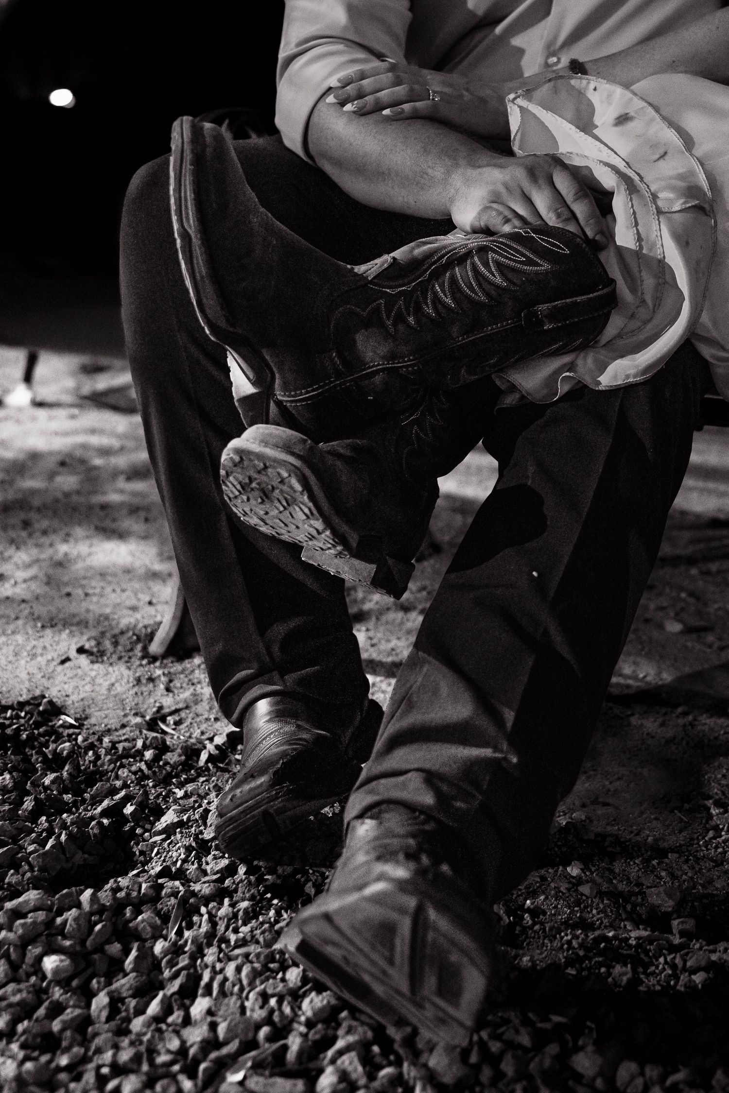 Black and white detail shot of worn boots and denim on gravel ground.