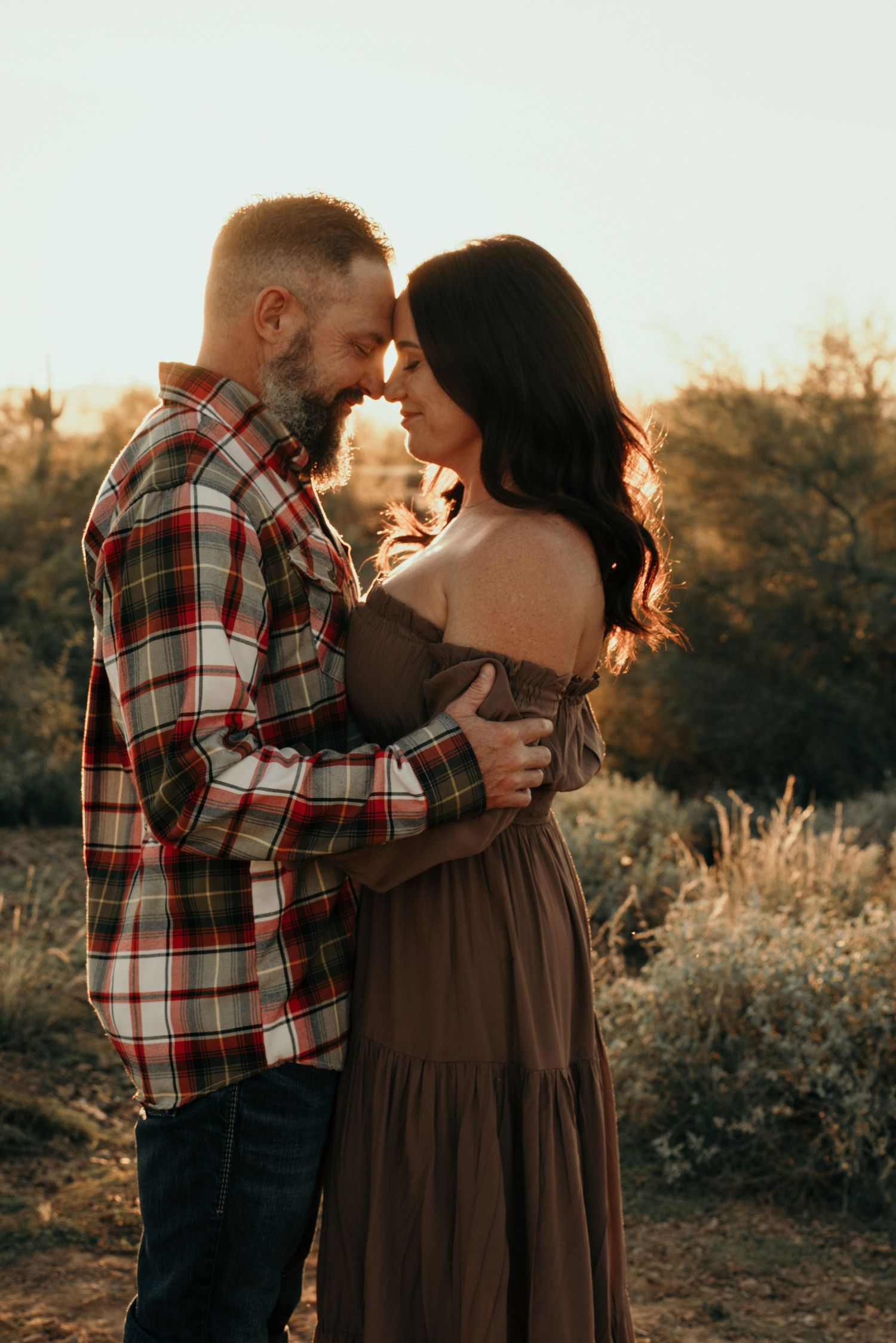 A romantic couple embraces at sunset in a desert landscape while wearing plaid and brown attire.