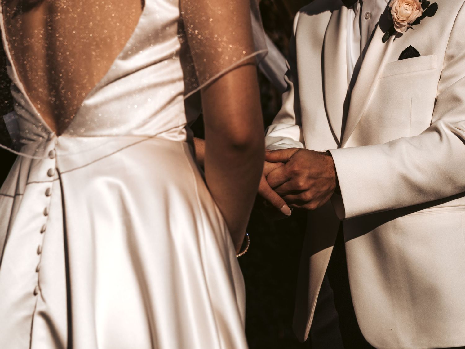 Close-up detail shot of elegant white wedding attire and clasped hands.