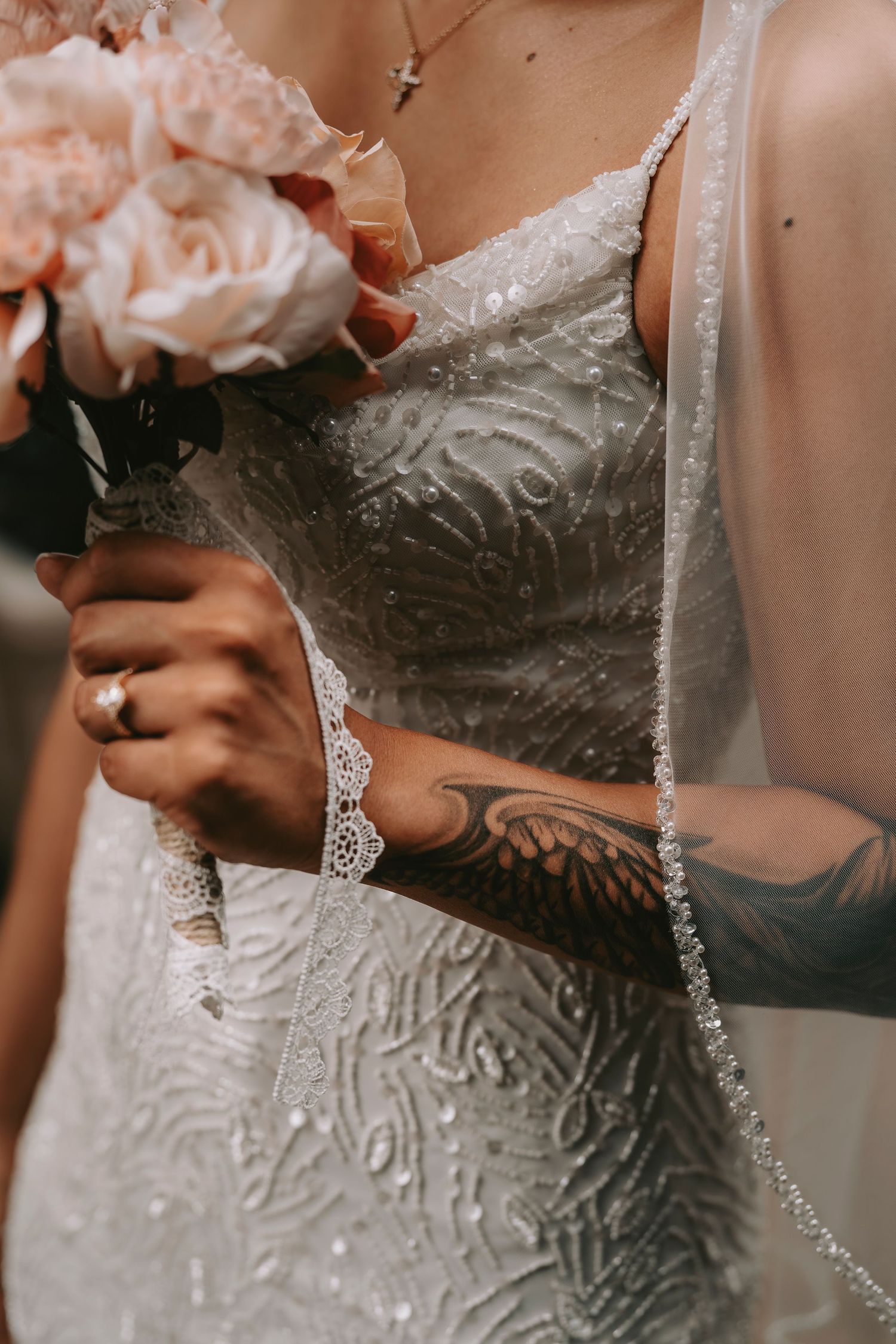 Close-up of lace wedding dress detail and bouquet with pink roses.
