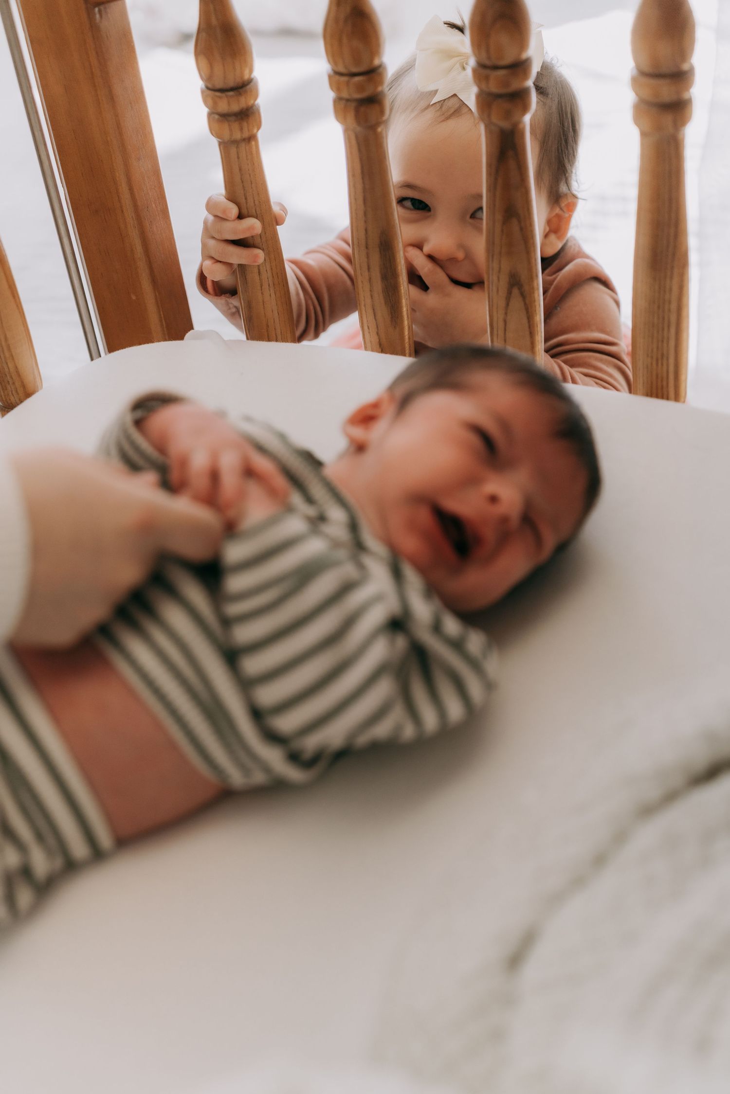 Two children playing and laughing together near wooden stair railings in a candid indoor moment.
