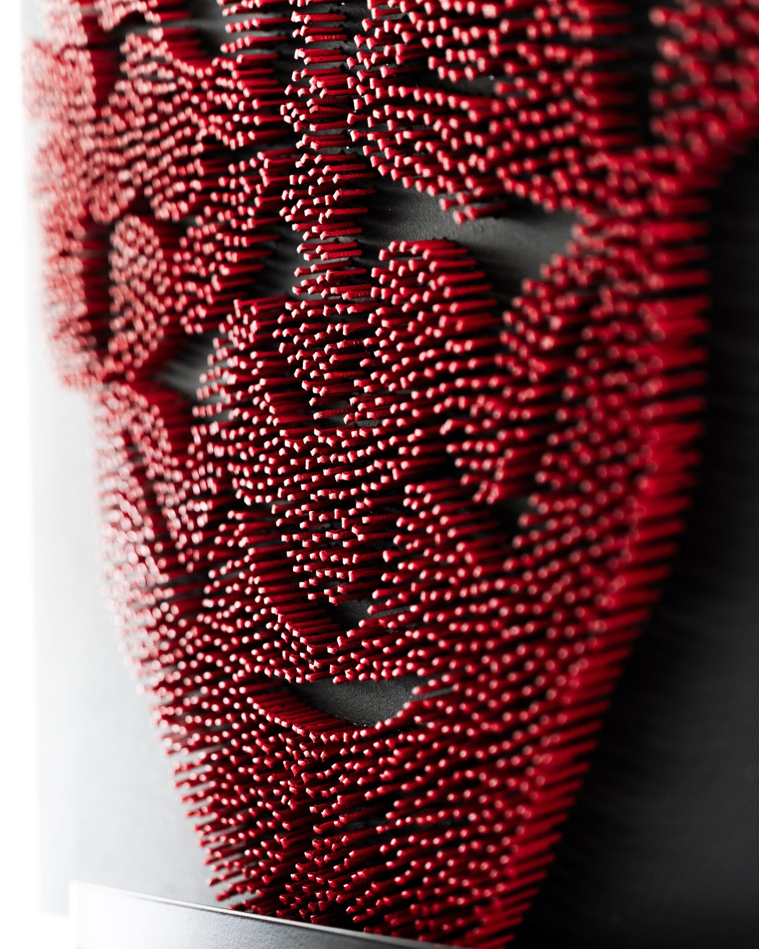 Close-up view of a bright red vase with rows of ornate, textured dotted patterns creating an intricate surface design.