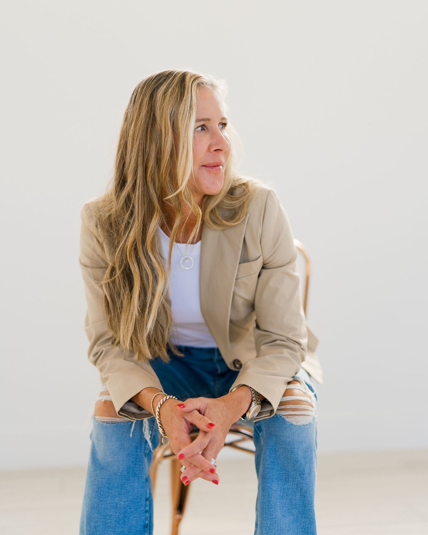 Professional portrait series showing person in beige blazer and jeans sitting casually on white background.
