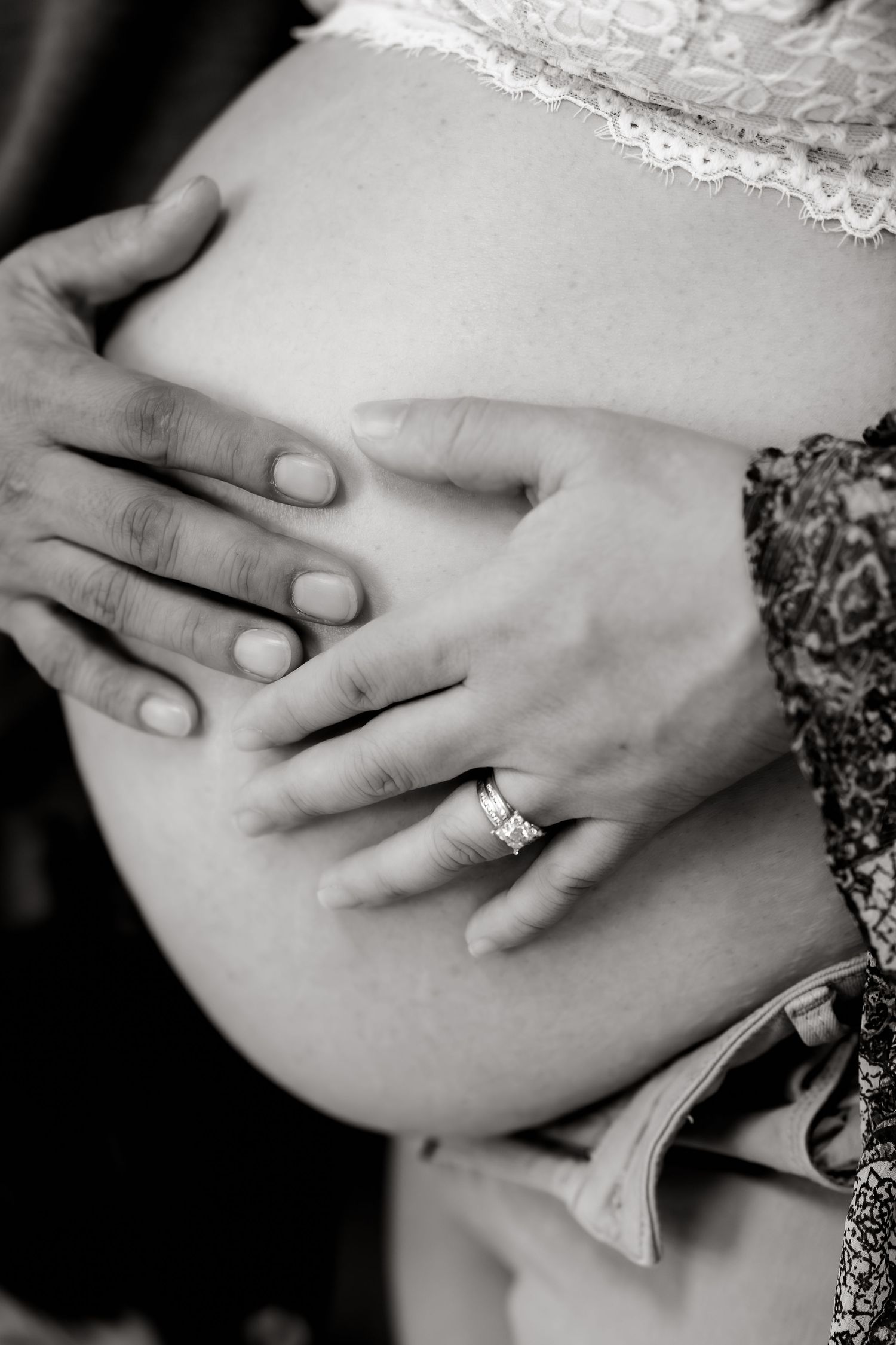 A series of black and white photos showing hands gently cradling a pregnant belly in lace maternity dress.