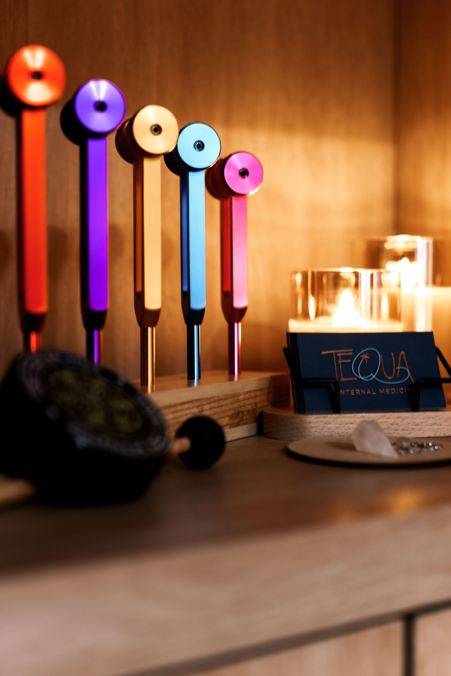 Colorful glowing light tubes arranged in a row cast warm illumination against a dark wall with candles in the background.