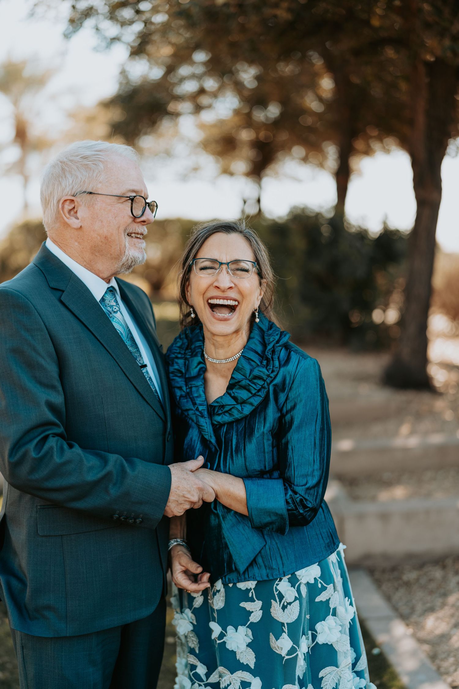 Elderly couple in matching blue outfits sharing candid laughter outdoors.