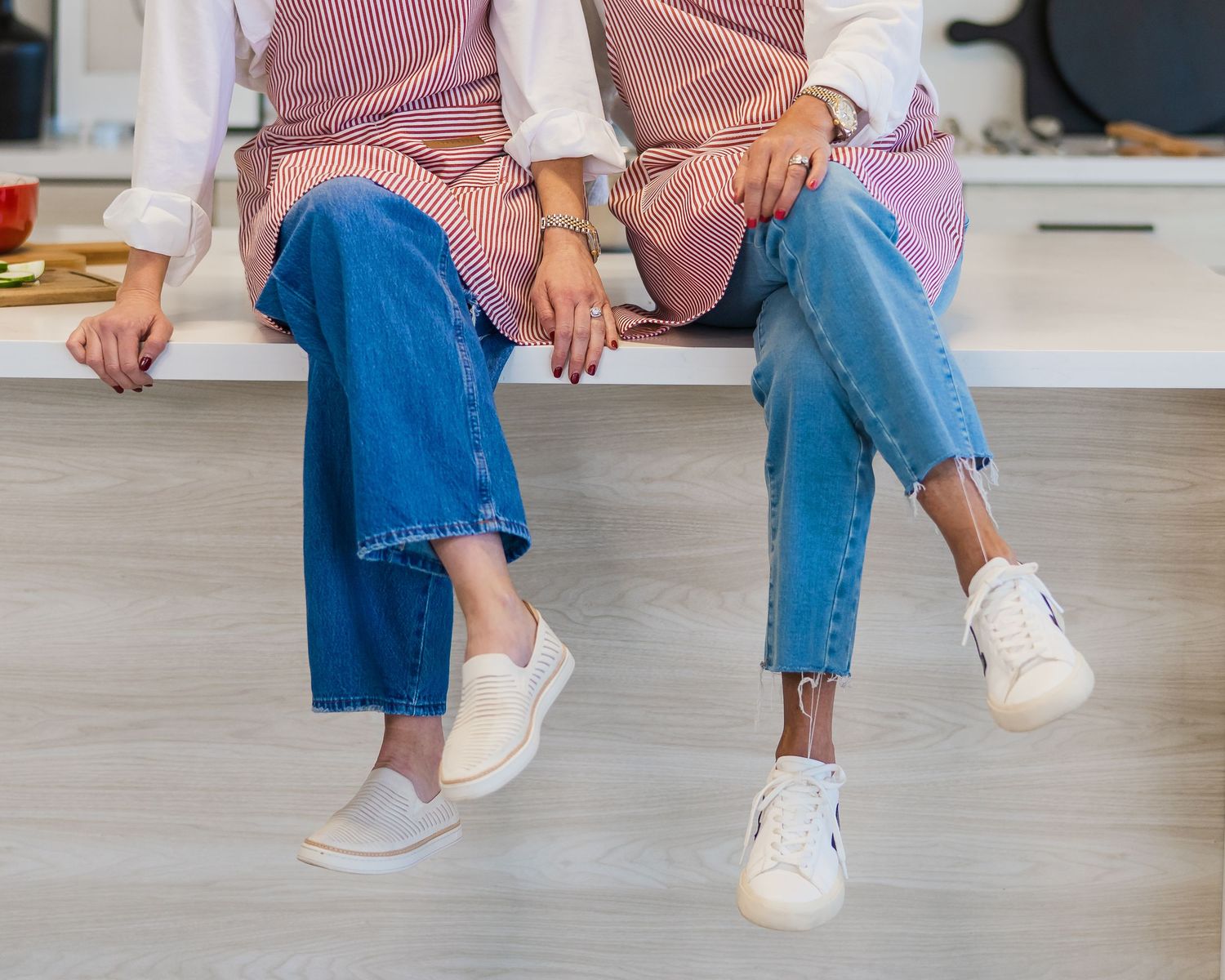 Row of people wearing jeans and white sneakers shown from waist down in casual standing poses.
