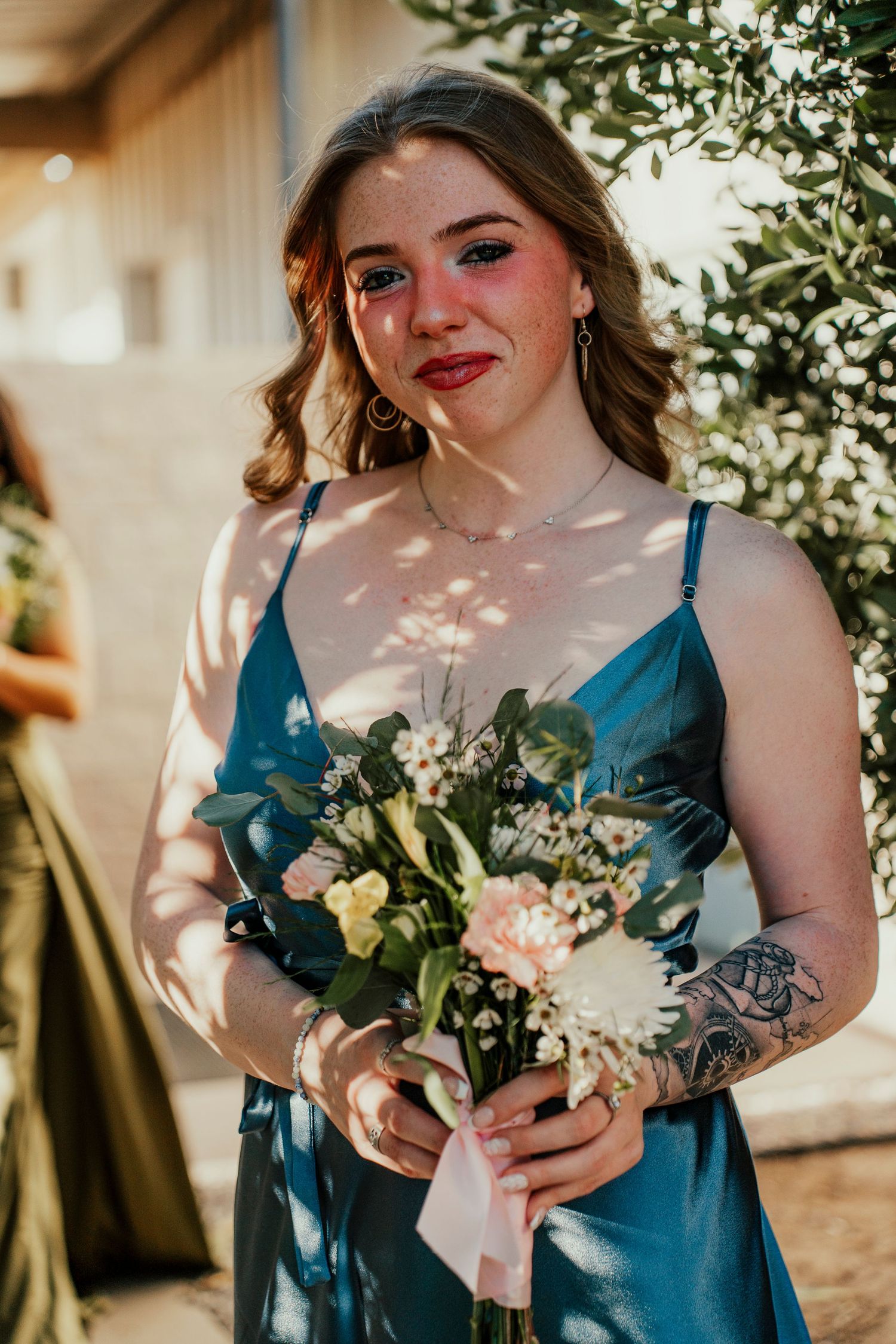 Bridesmaid in teal dress holds a delicate bouquet of white and peach flowers.