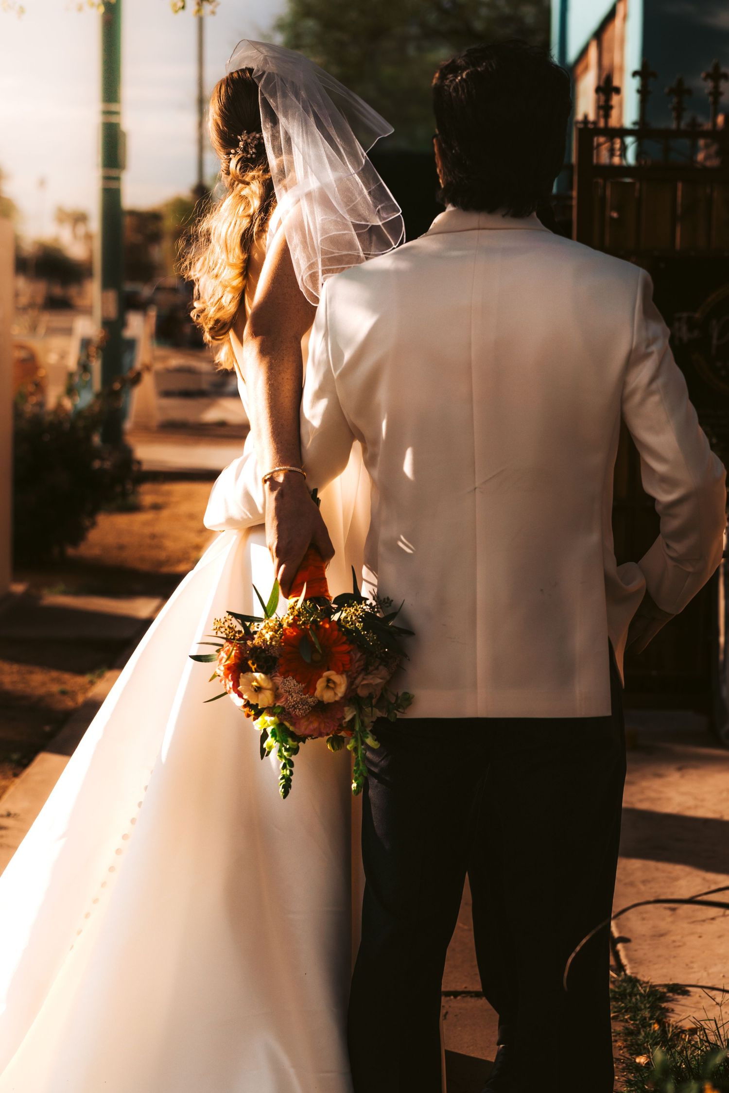 Silhouetted wedding couple with bouquet against golden sunset light.