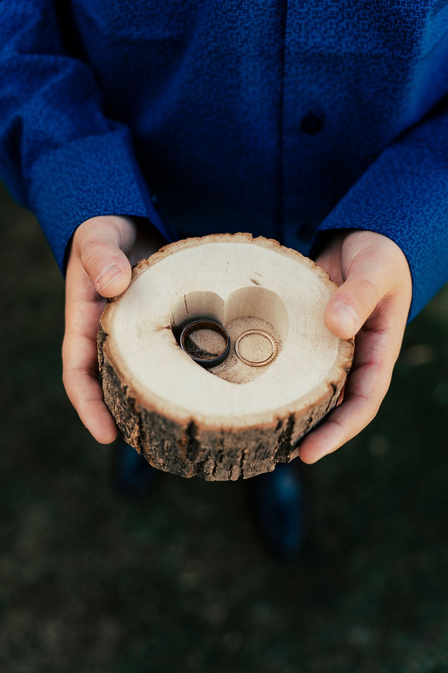 Wedding rings displayed on a natural wood slice ring holder with rustic bark edges.
