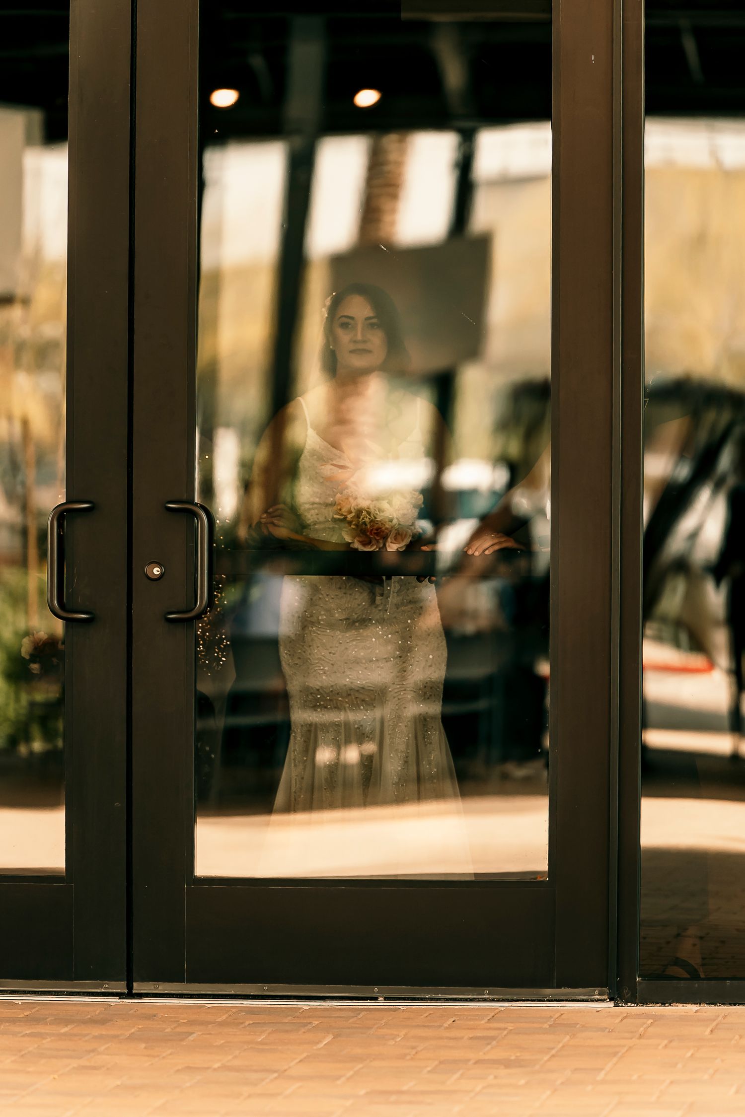 Reflection of person in wedding dress through glass doors at sunset.