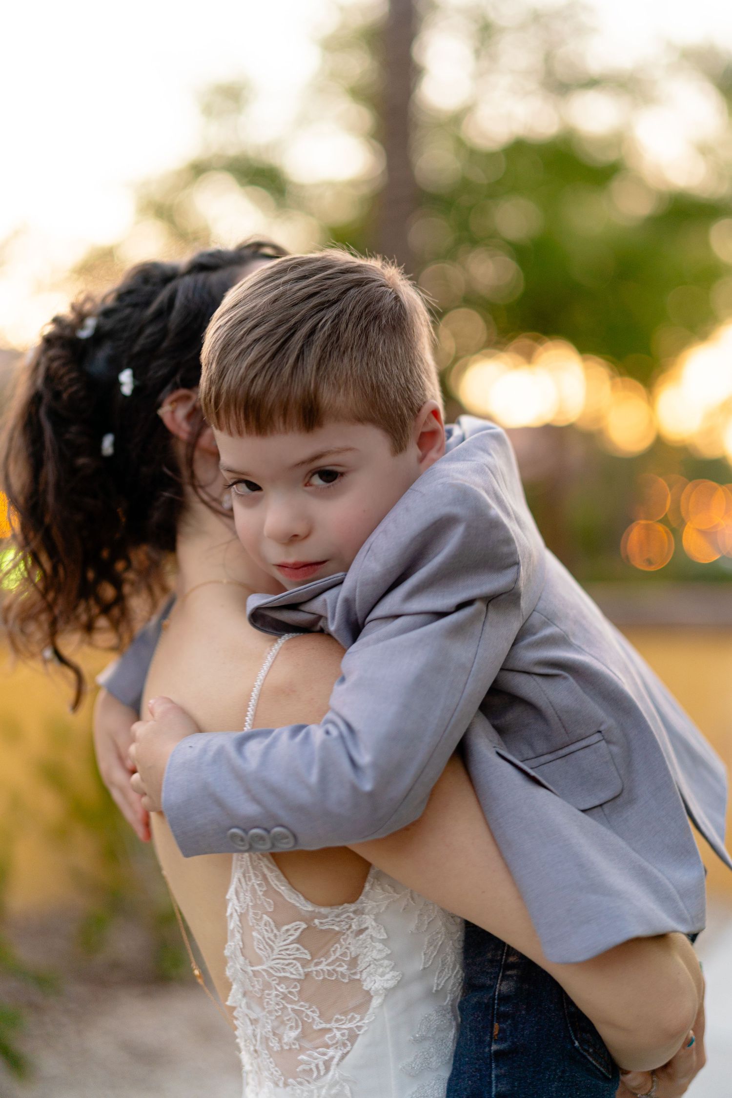 Heartfelt embrace during outdoor wedding photoshoot with gray suit and lace dress.